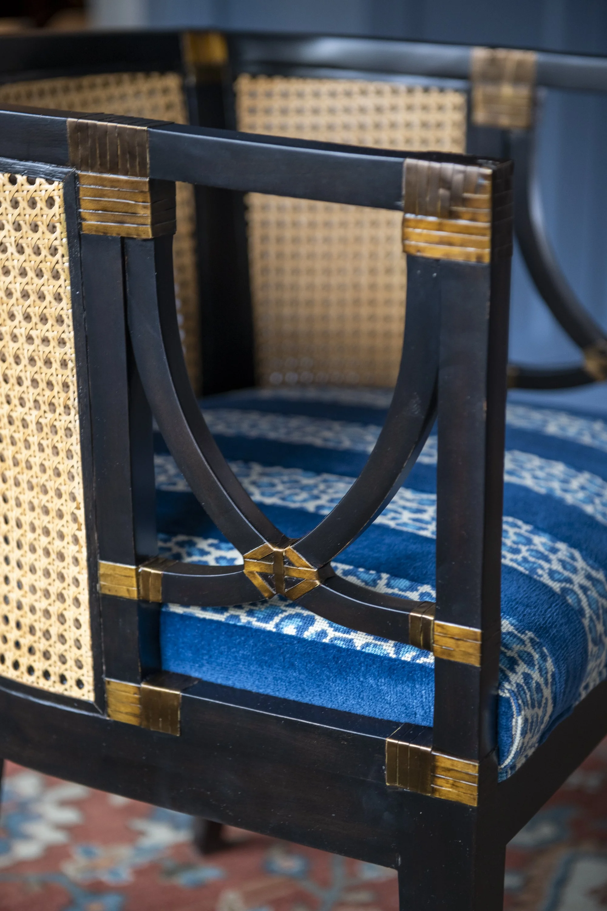Close-up of a black wooden chair with woven rattan details on the backrest, sitting on a blue patterned carpet.