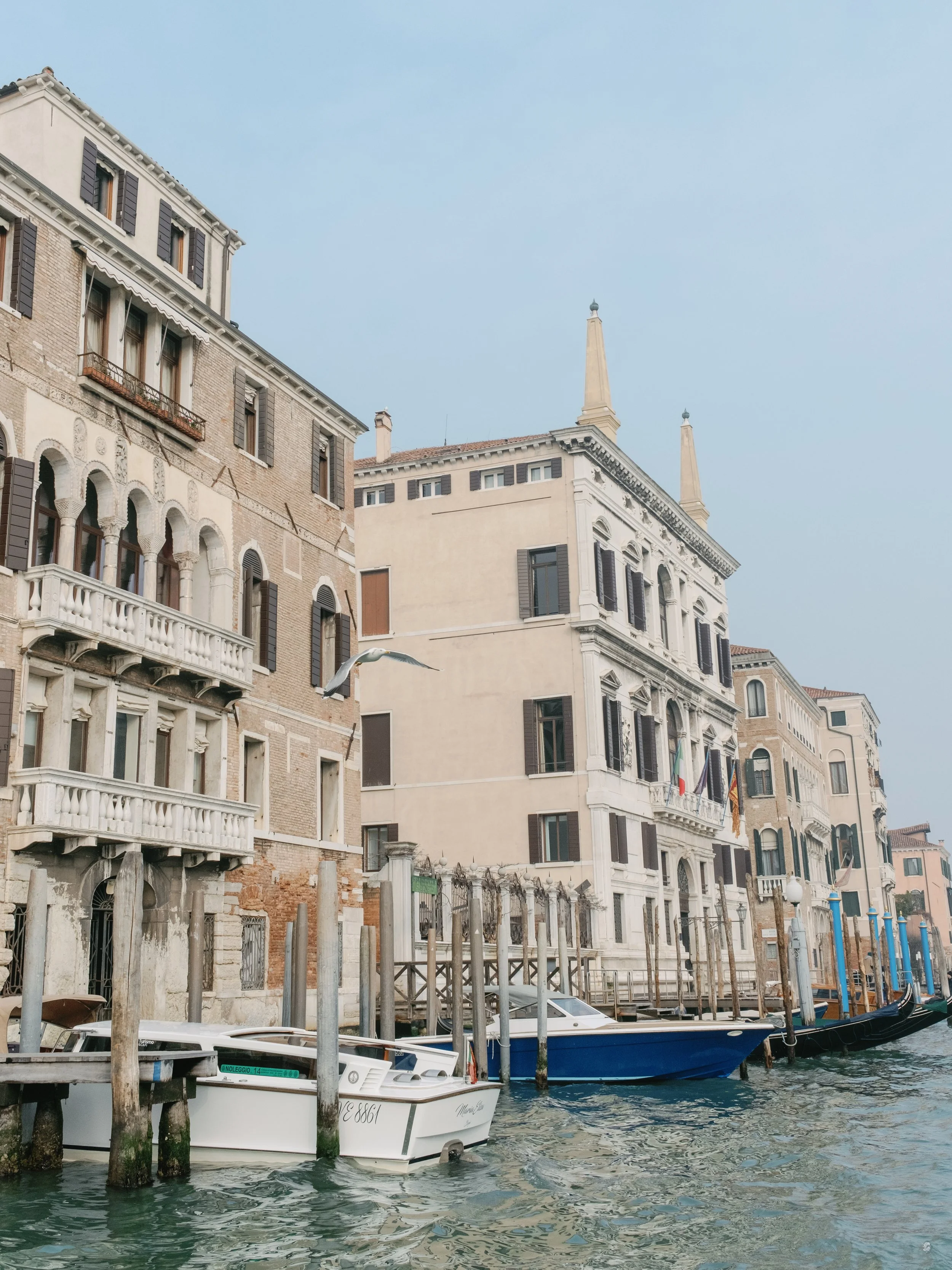 View of historic buildings along a canal in Venice, Italy, with boats docked at the water's edge.