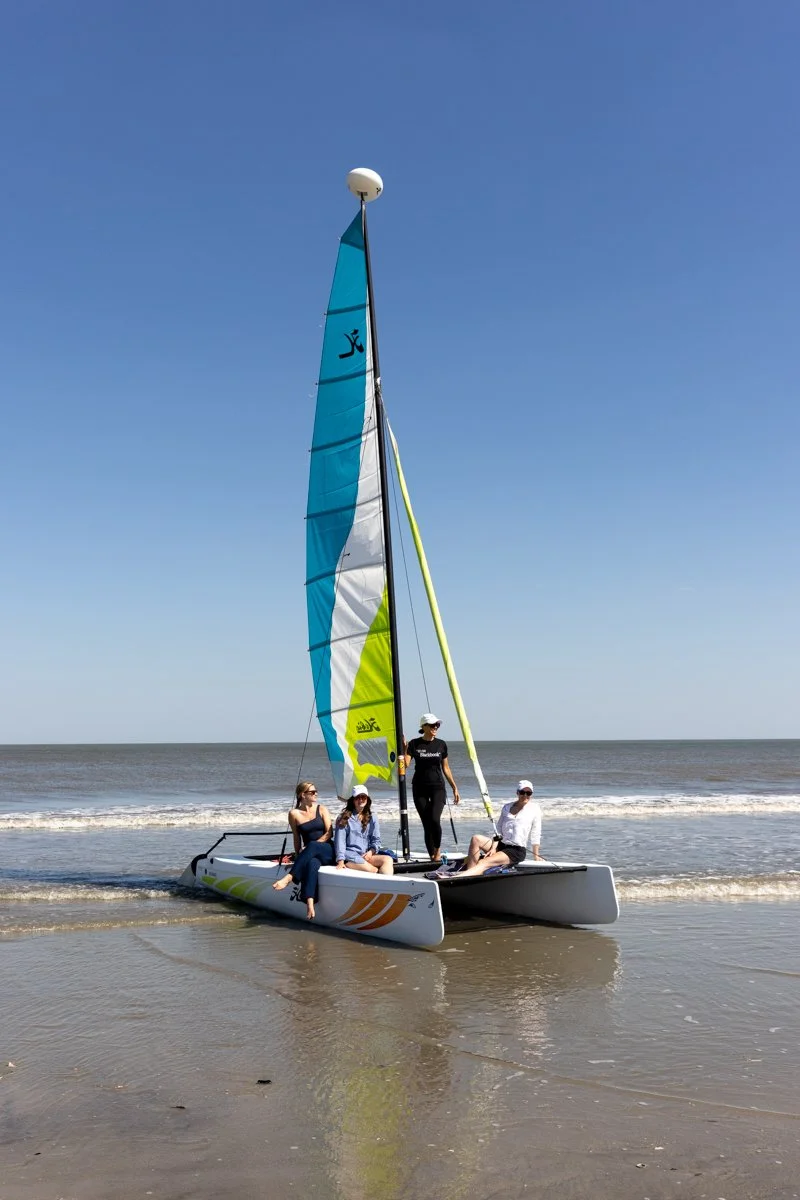 Four people on a sailboat near the shore with a blue sky in the background at Sea Island Resort in Georgia.