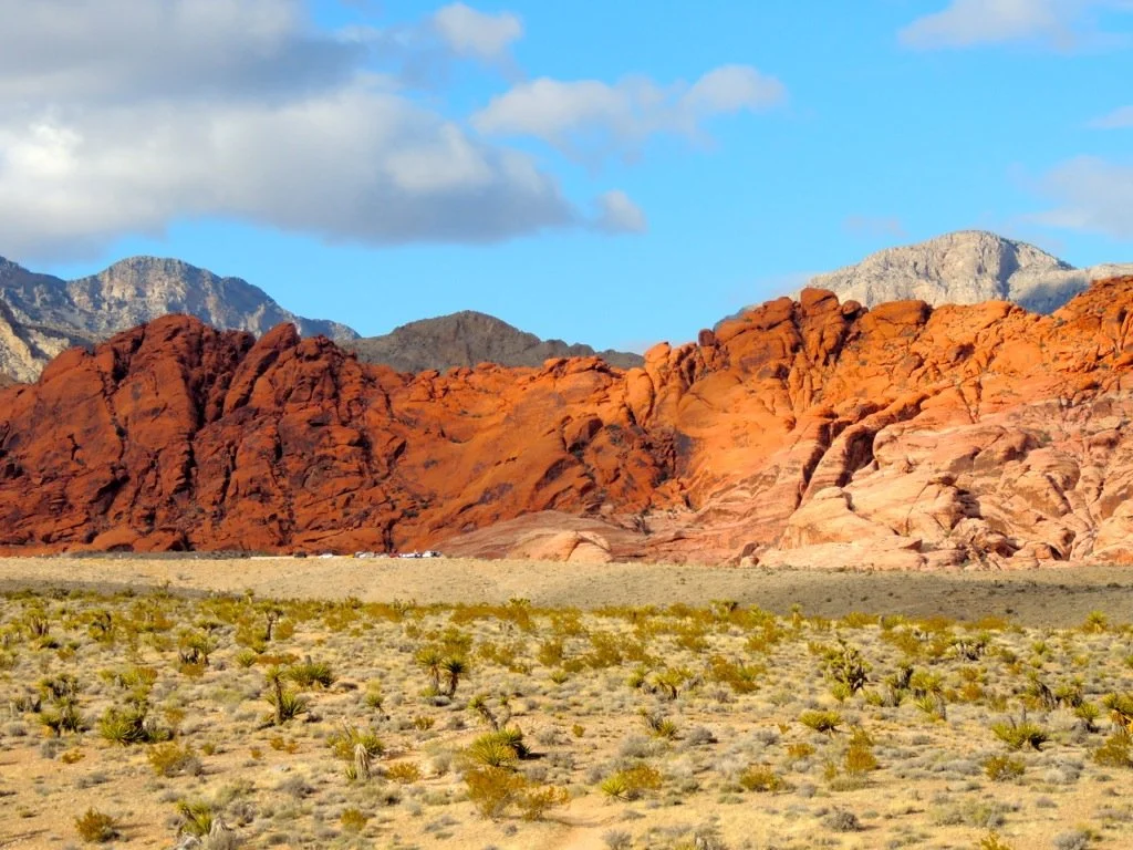 some clouds in the blue sky and dramatic red colored rock mountain with scrubby plains in front