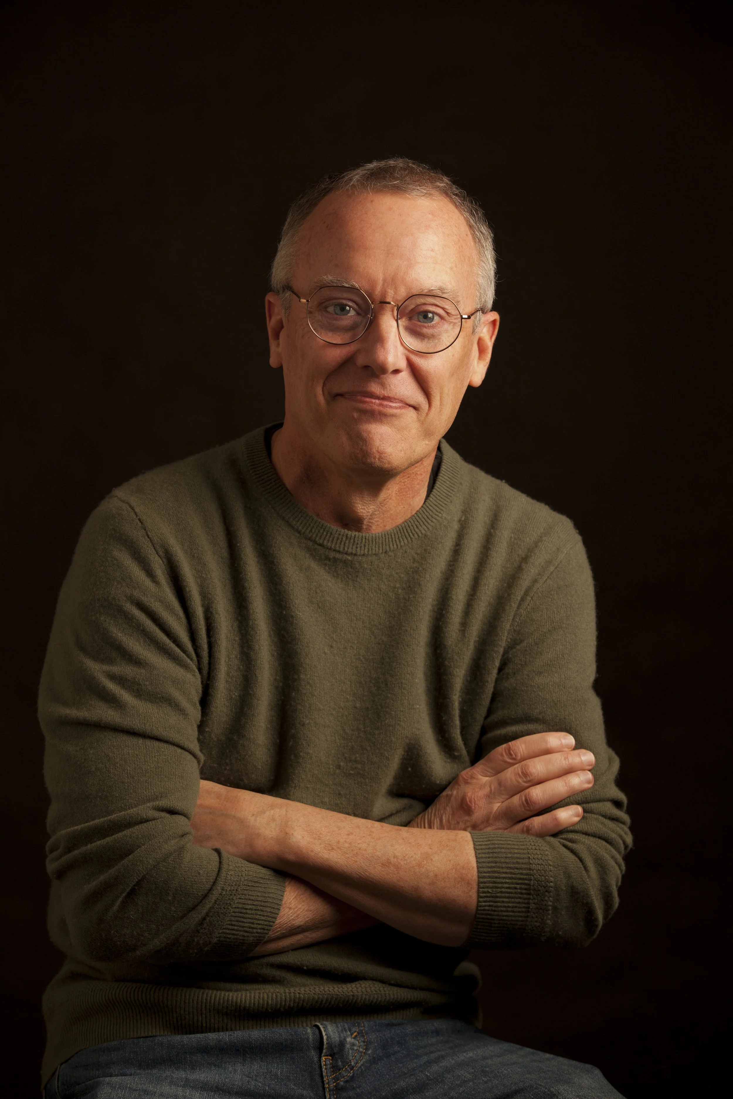 Author Dave Kenney wearing glasses and a green sweater on a dark background.