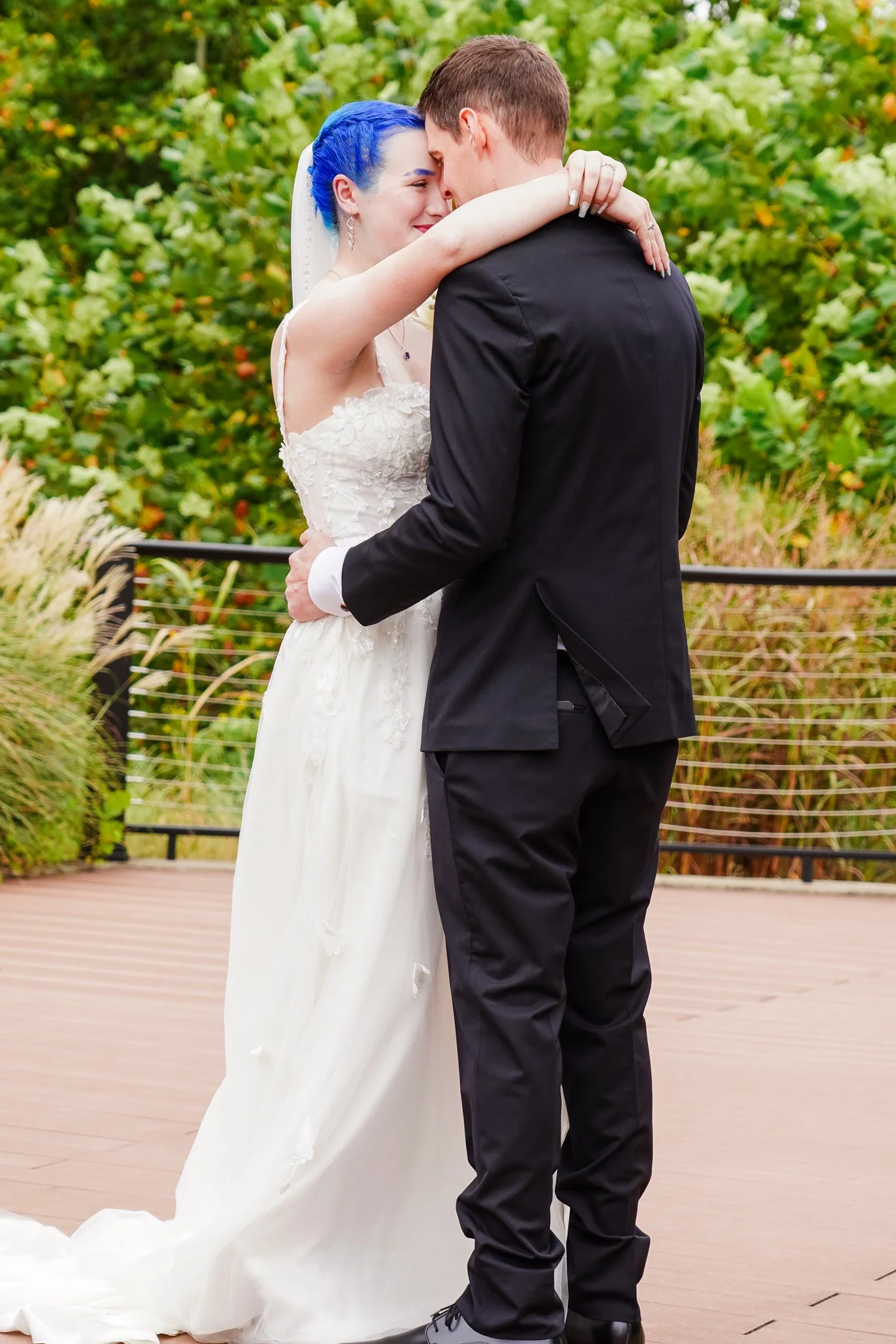 A bride and groom close together, smiling and touching foreheads, during their outdoor wedding ceremony with green foliage in the background.