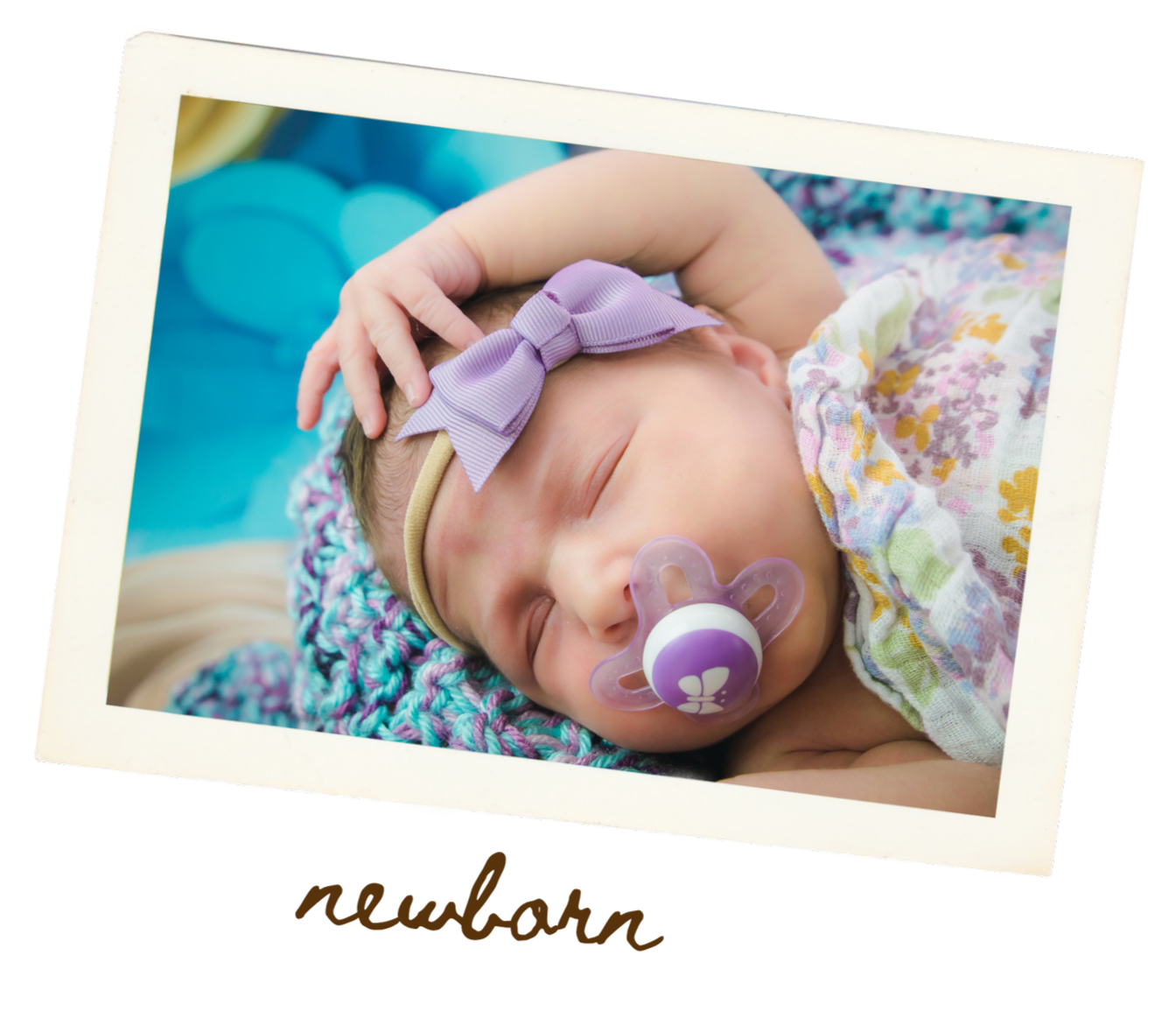 A sleeping newborn baby with a purple bow headband and a pacifier, lying on a multicolored blanket.
