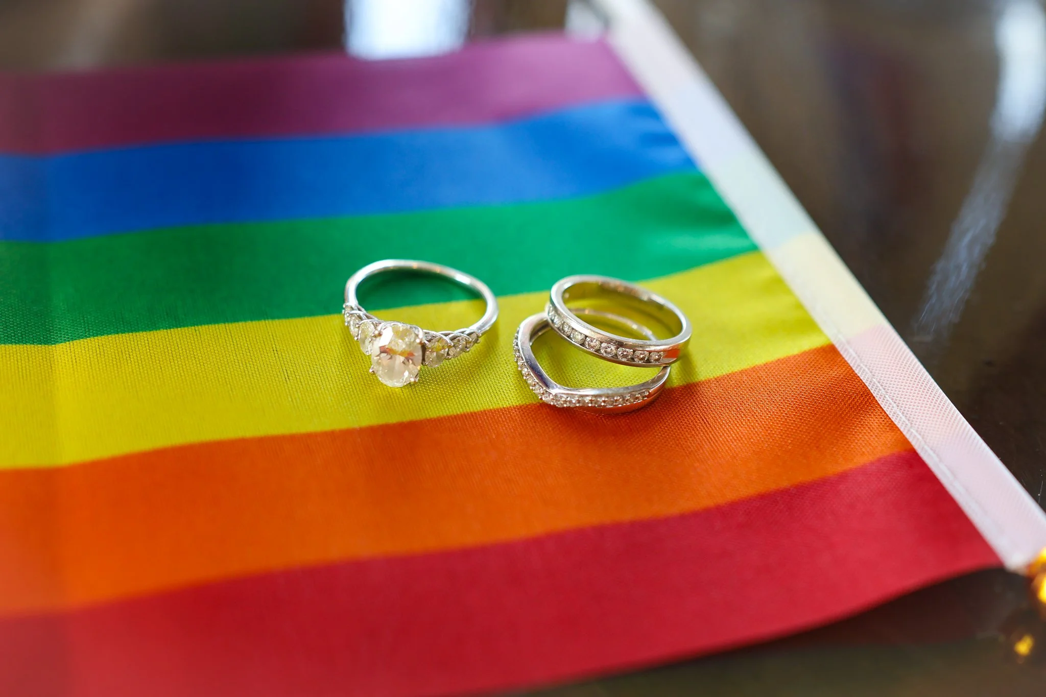 Three silver rings with gemstones placed on a rainbow Pride flag fabric.