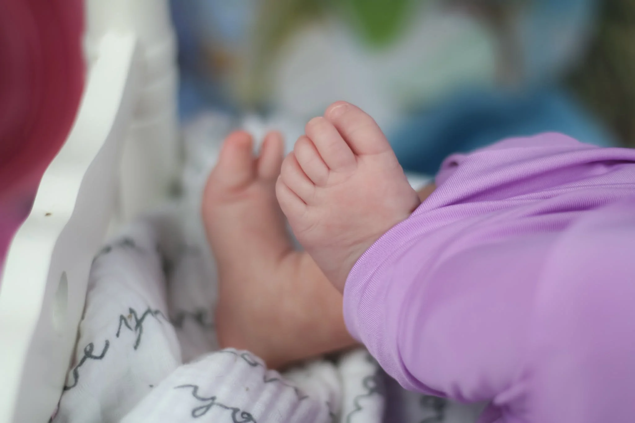 Close-up of a child's hand holding an adult's hand, both with light skin, with the child wearing a purple sleeve and the adult wearing a white sleeve with black and grey writing.