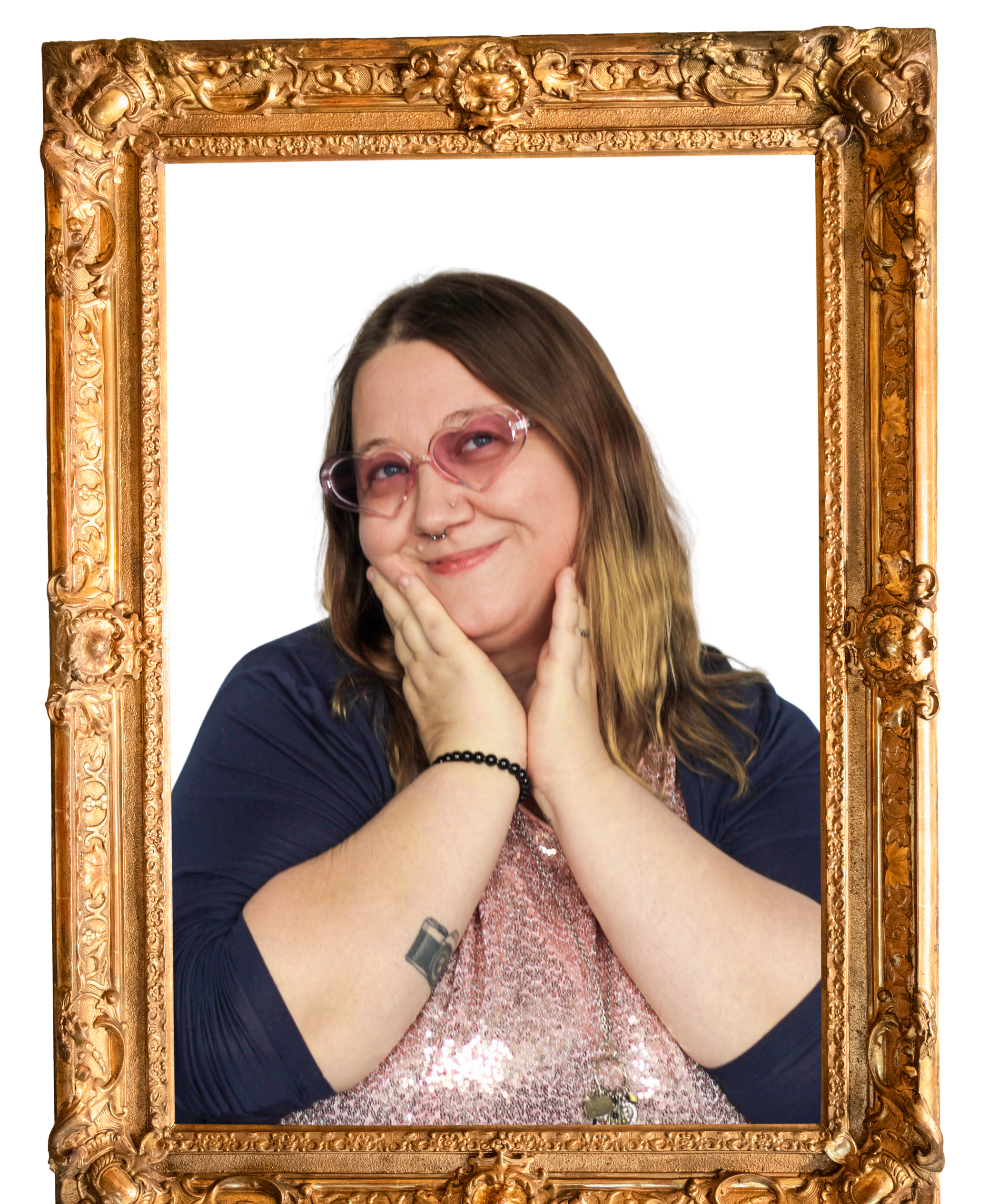 A young woman with light skin, long hair with blonde tips, wearing pink glasses, posing with a hand on her chin and a smile, in front of a gold ornate picture frame.