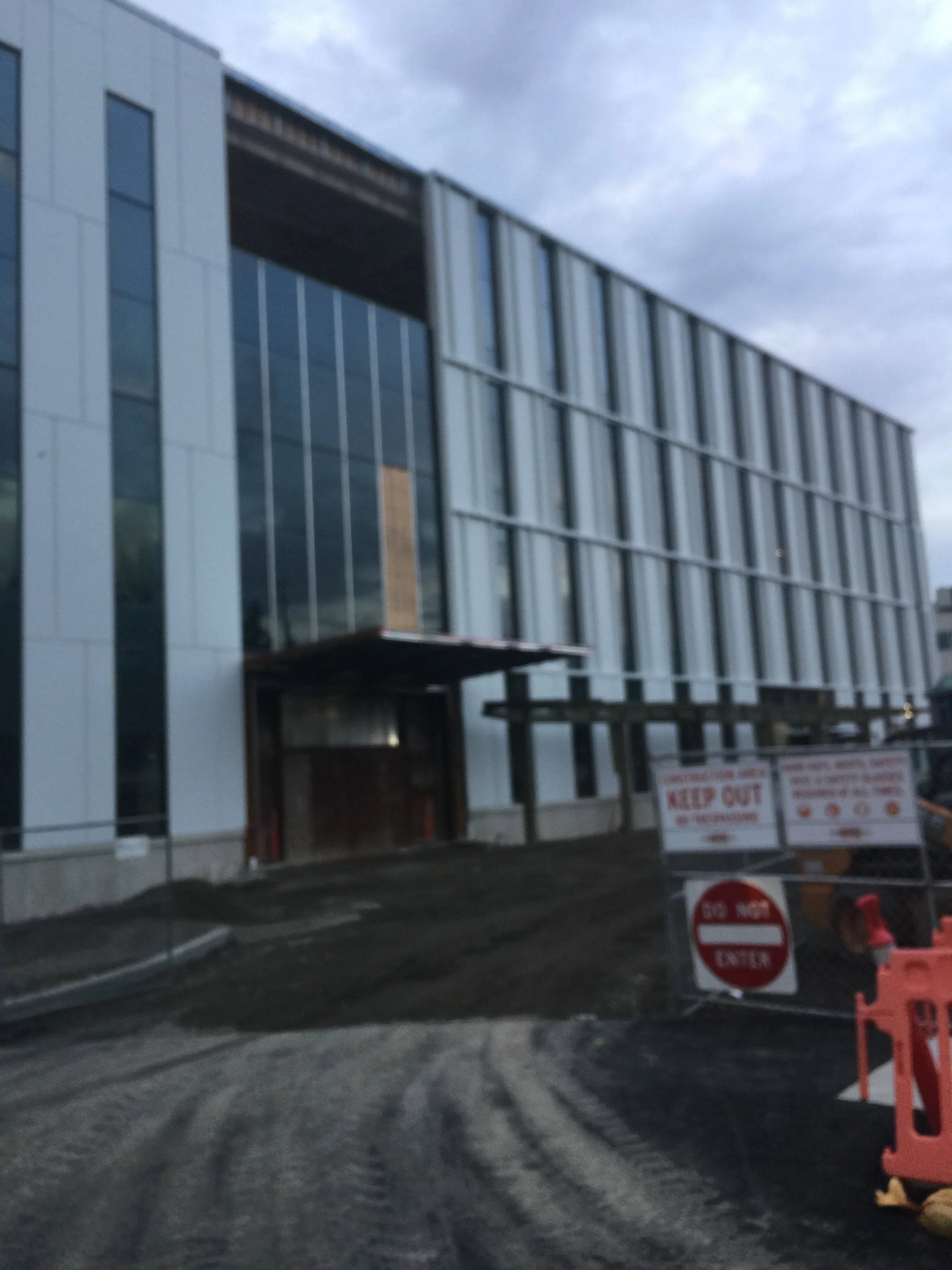 Construction site with a modern multi-story glass building, dirt road, and warning signs including 'Keep Out' and 'Do Not Enter'.