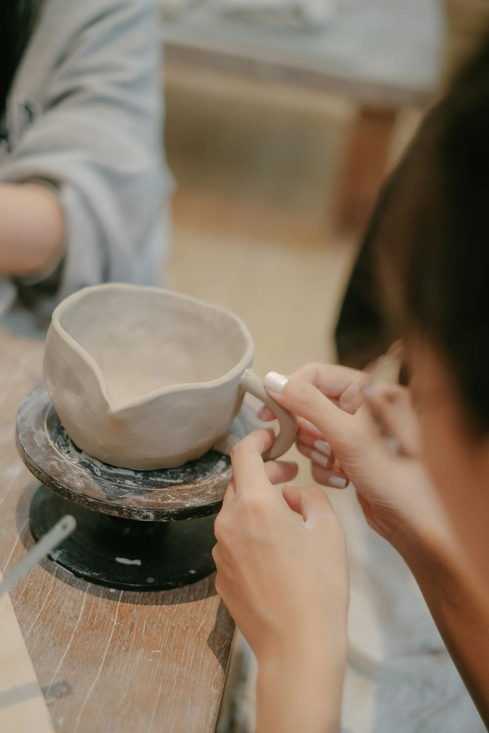 Person shaping a ceramic mug on a pottery wheel in a ceramics studio.