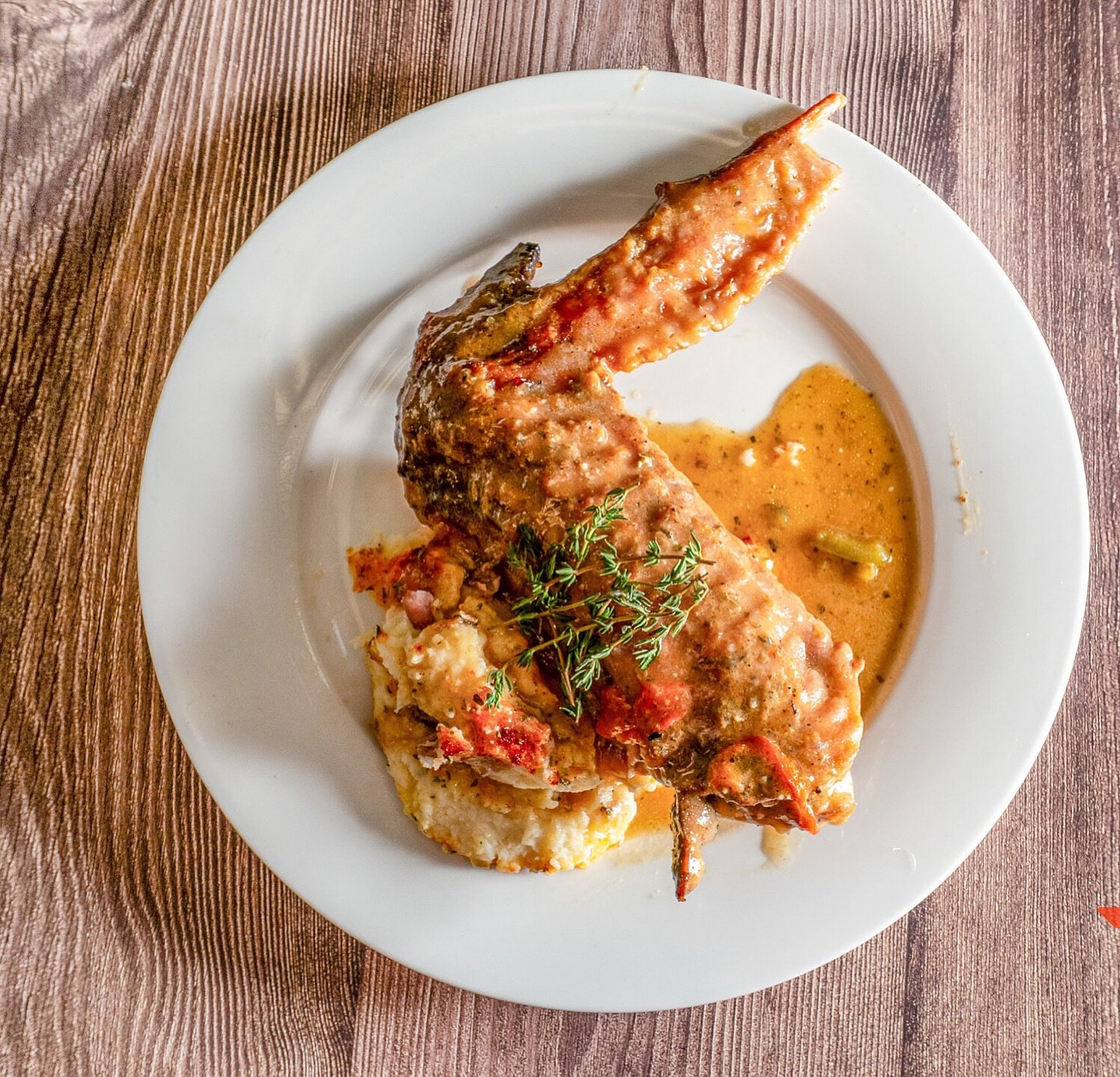 A plate of cooked fish with sauce, garnished with herbs, served with mashed potatoes, on a wooden table.