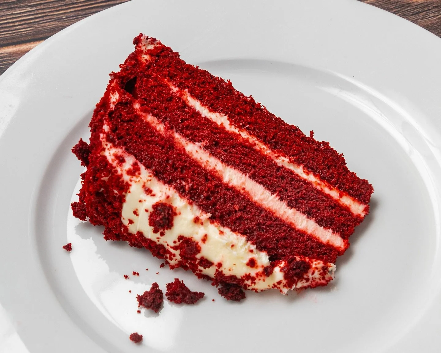 Slice of red velvet cake with cream cheese frosting on a white plate.