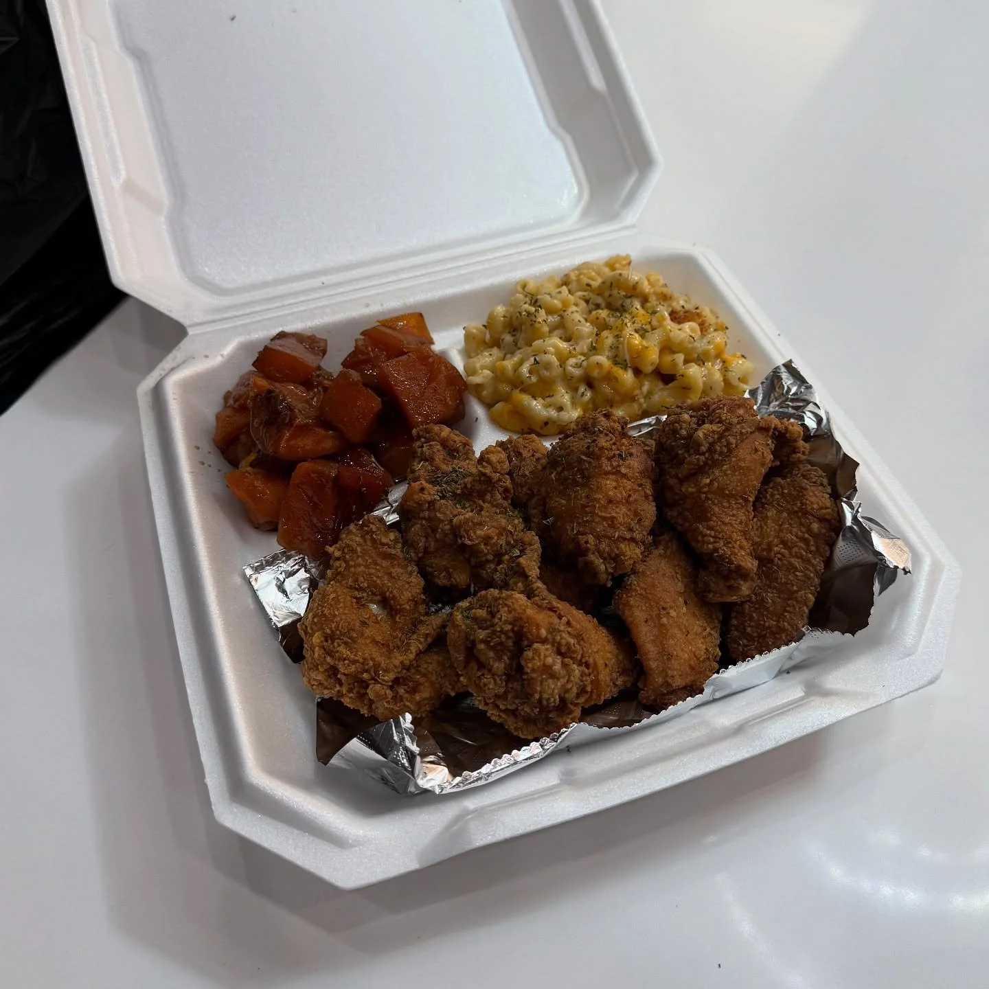 Fried chicken wings, macaroni and cheese, and diced sweet potatoes in a takeout container.