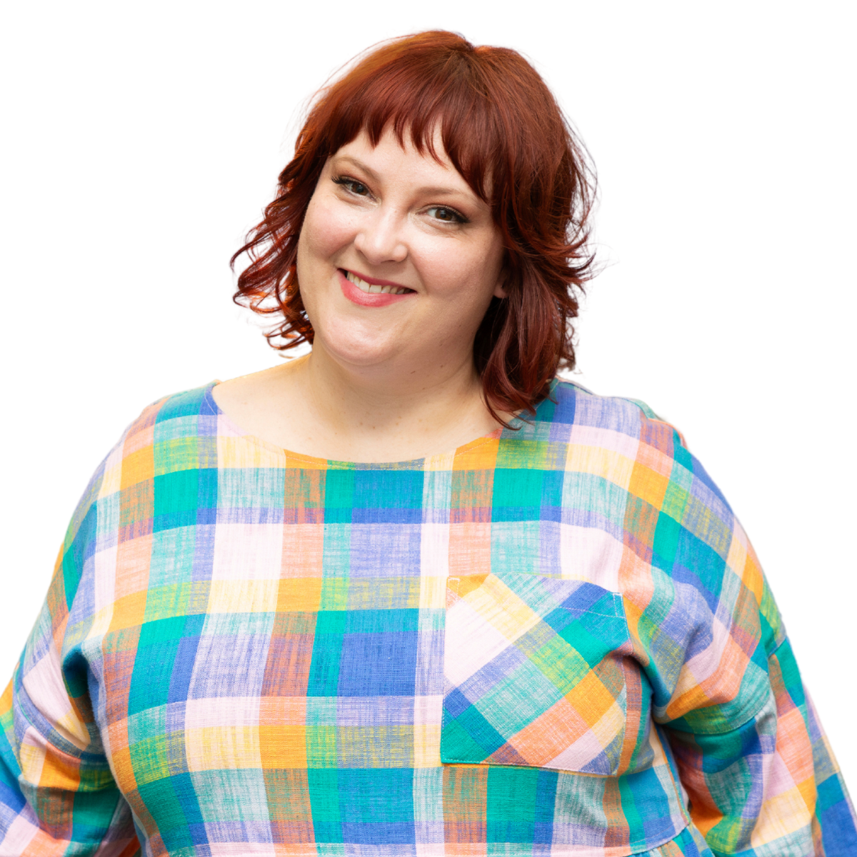 Photo of Felicity smiling at the camera. She has short red wavy hair and wears a bright checked shirt.