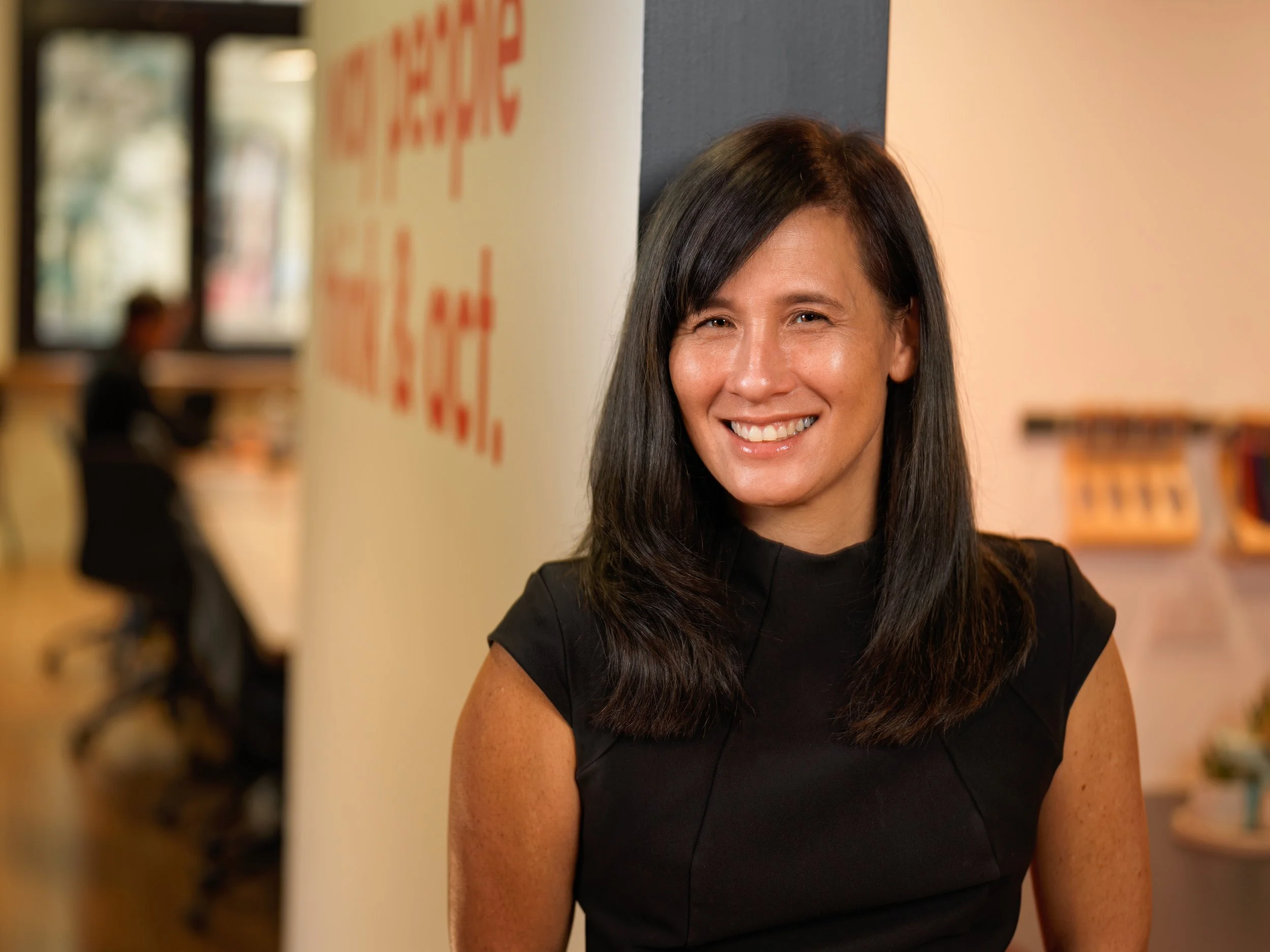 Photo of Amanda Newbery smiling at the camera. She has long dark hair that is loose, and wears a dark sleeveless shirt.