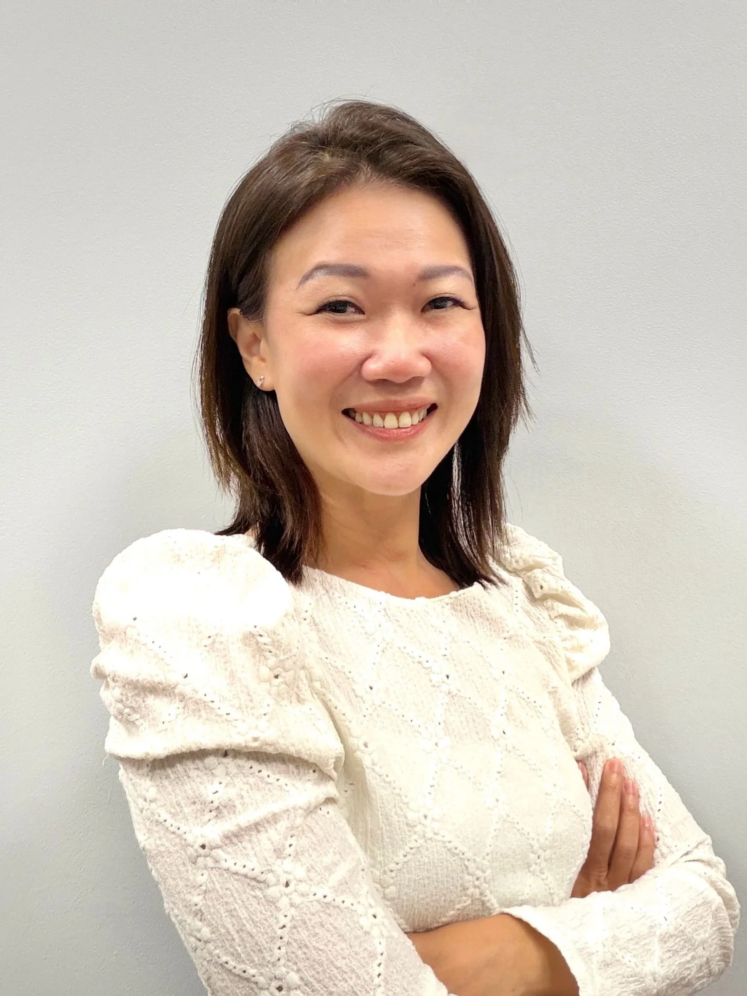 Photo of Lyn smiling at the camera. She has short dark straight hair, and wears a white shirt.