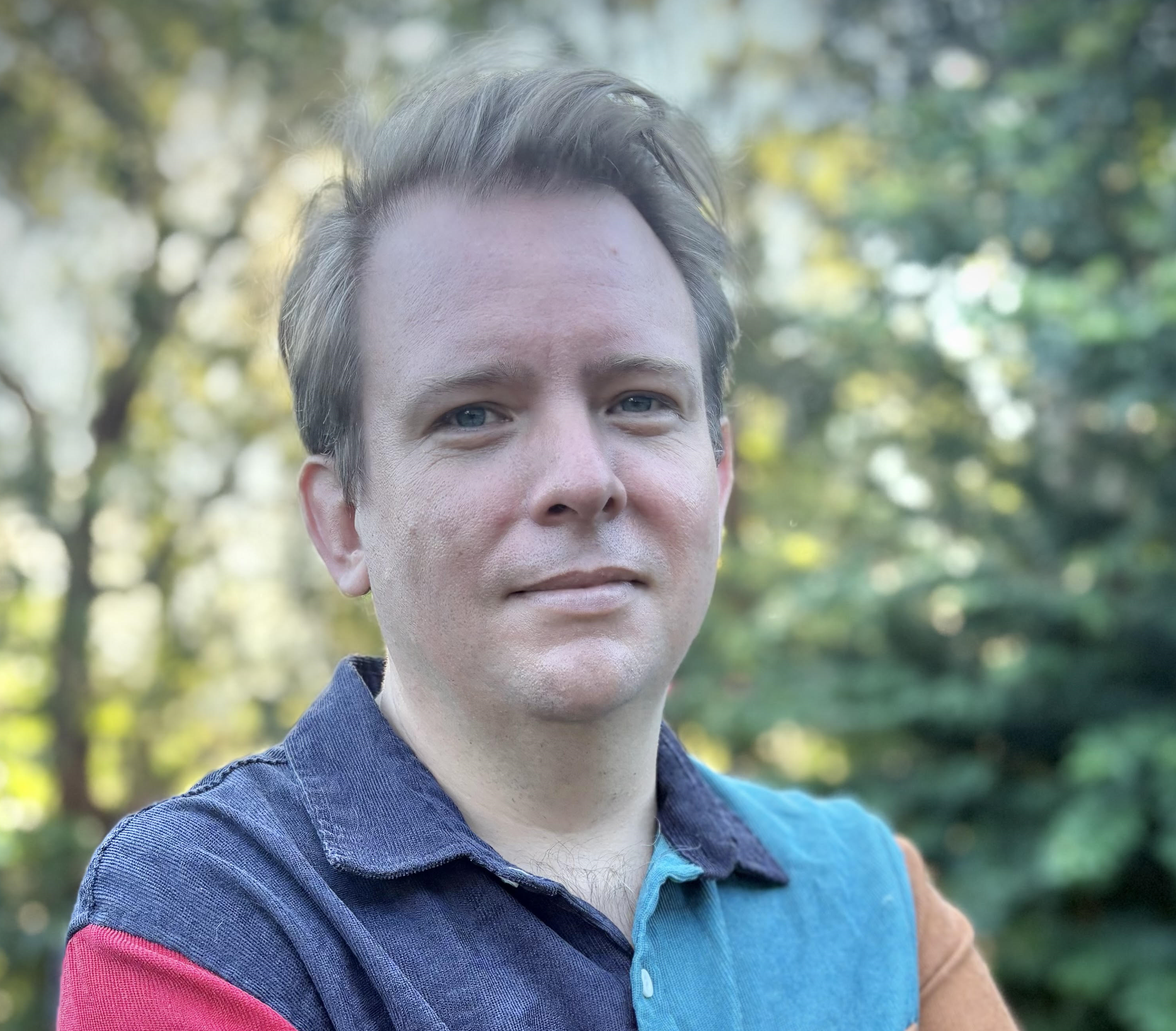Photo of Mitch looking at the camera. He has short light-coloured hair, and wears a bright-coloured collared shirt