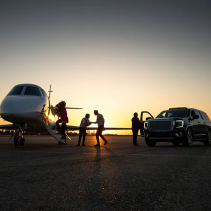 People boarding a private jet at sunset, with a black SUV parked nearby.