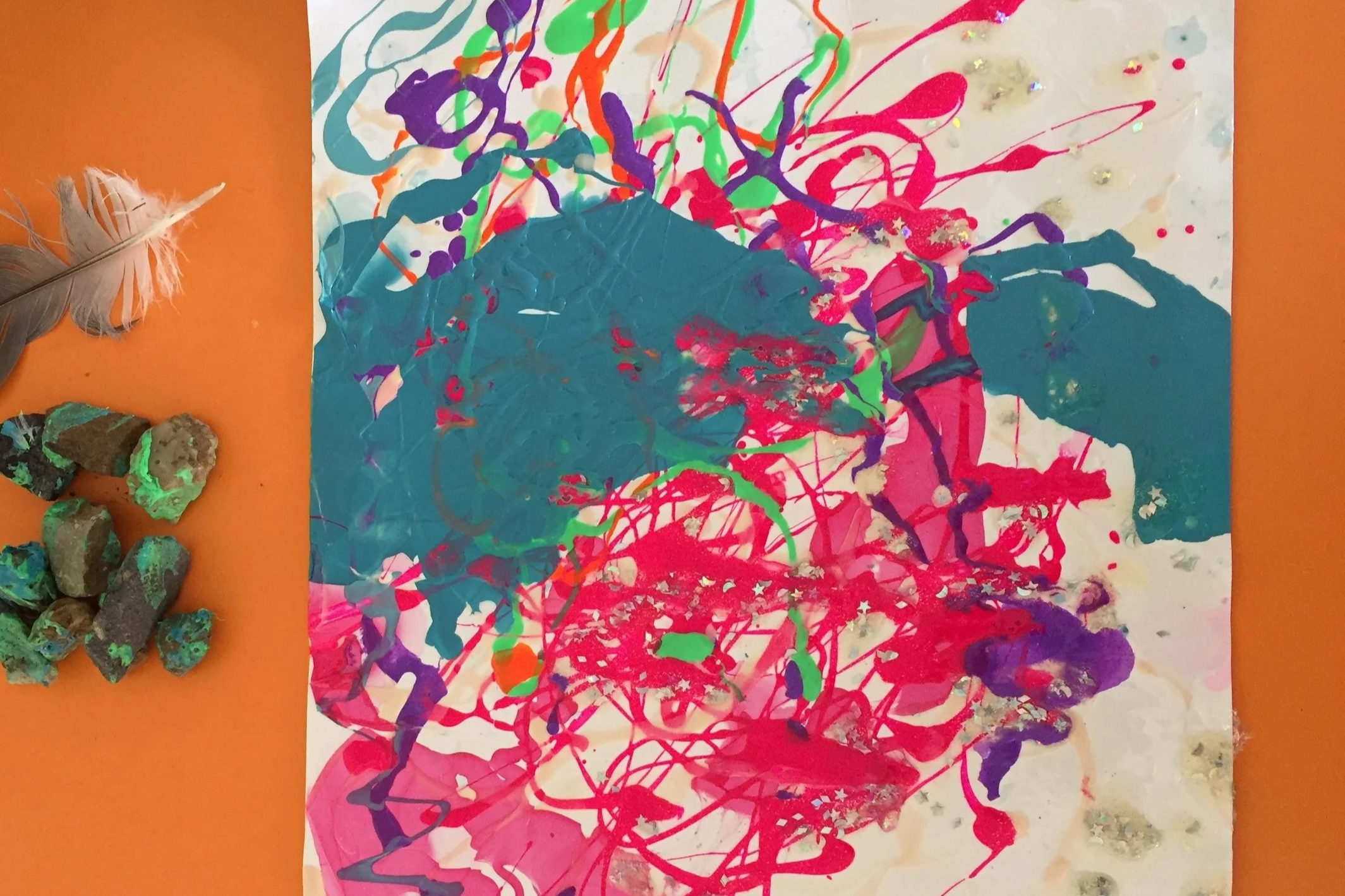 Colorful abstract painting with splashes of pink, purple, green, orange, and dark blue paint on paper.