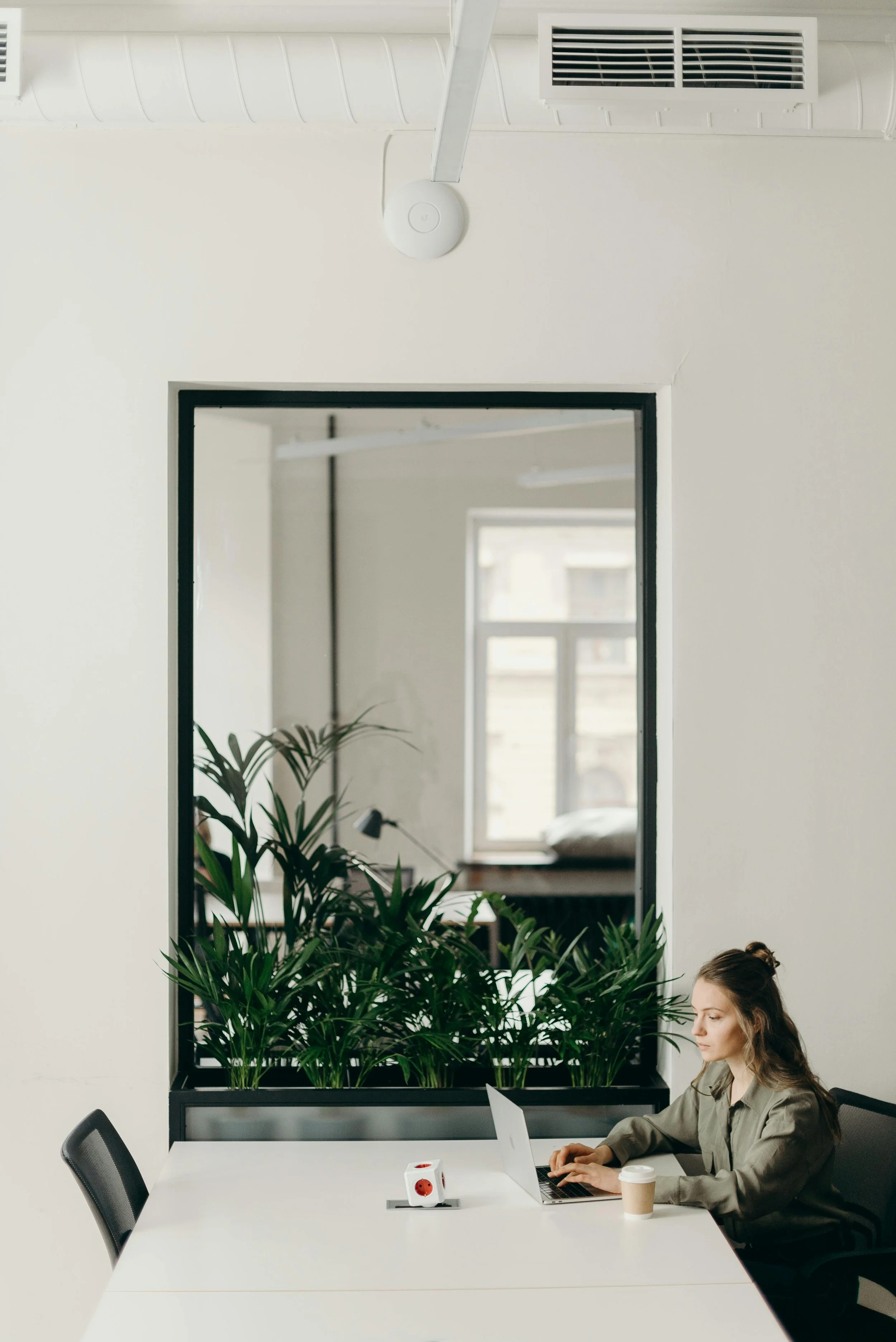 woman sitting at a long white table typing on a laptop.