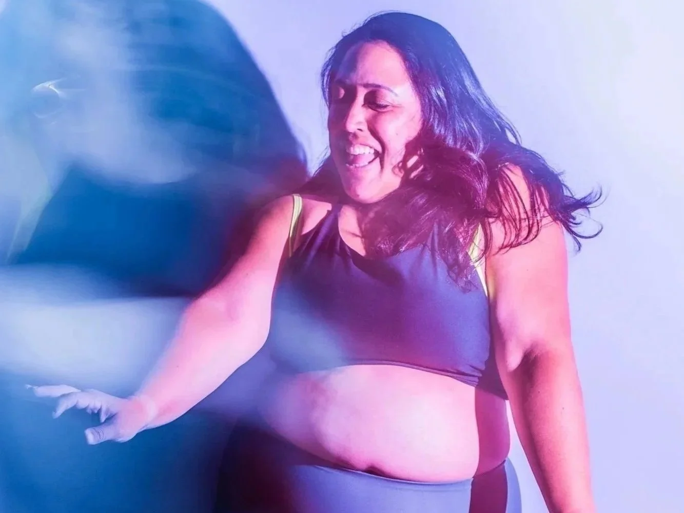 Plus size dancer moves and smiles casting blue shadows on a white wall