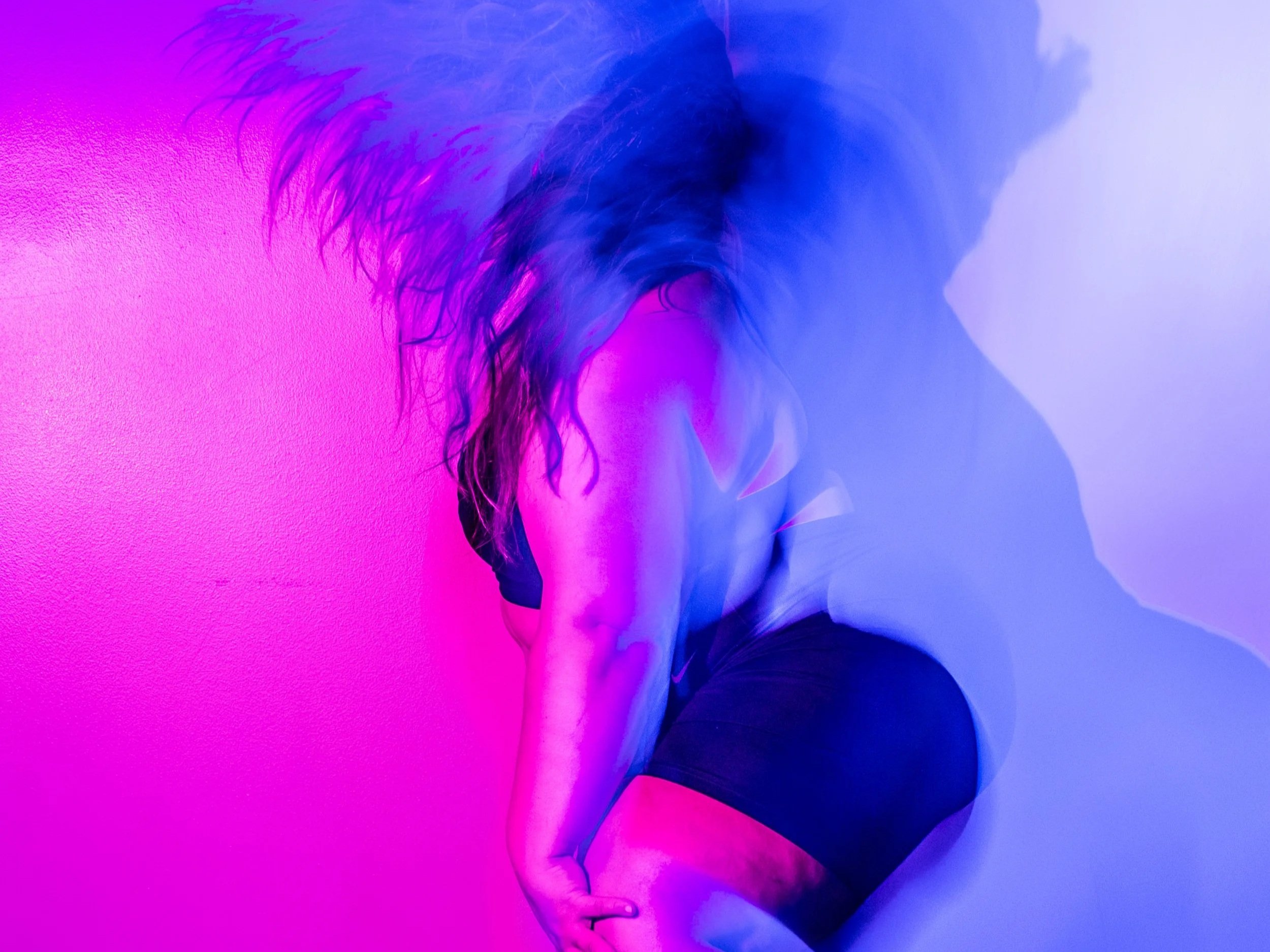 Plus size dancer flips hair in motion with blue and purple lighting behind