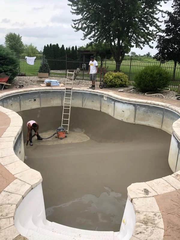 Workers are prepping an empty inground swimming pool for liner replacement.