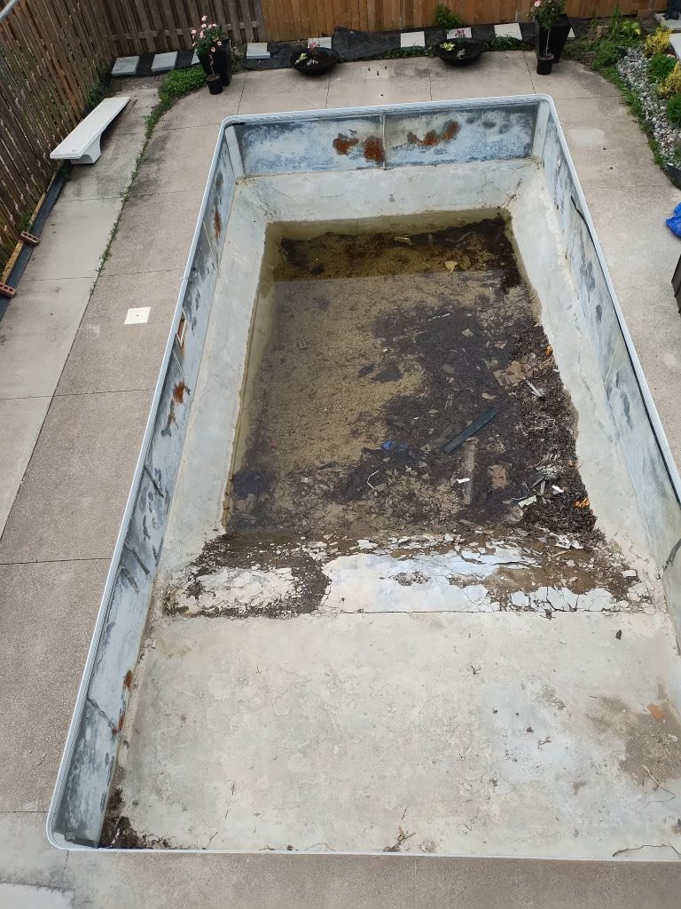 An empty inground swimming pool that is getting a new pool liner installed.