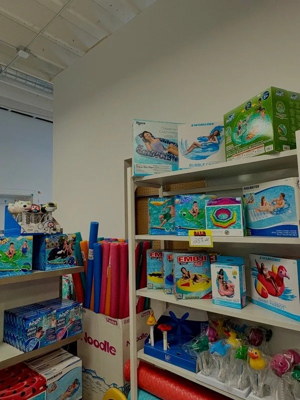 Retail store shelf displaying pool toys and inflatables, including foam mats, floating rings, and swimming accessories.