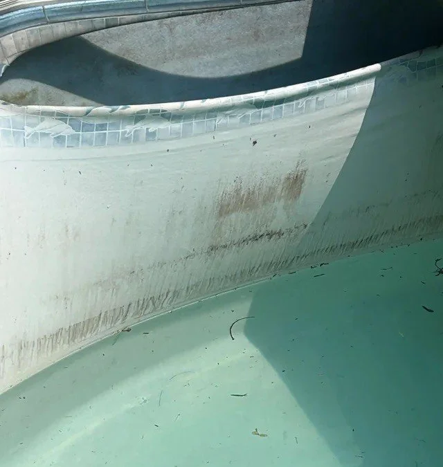 Close-up of the interior wall of an empty swimming pool showing a torn liner, with dirt and stains near the waterline.