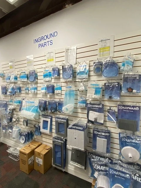 Display of plumbing and hardware parts on a wall shelf labeled 'Inground Parts', including skimmer parts, chlorinator parts, gaskets, and baskets.