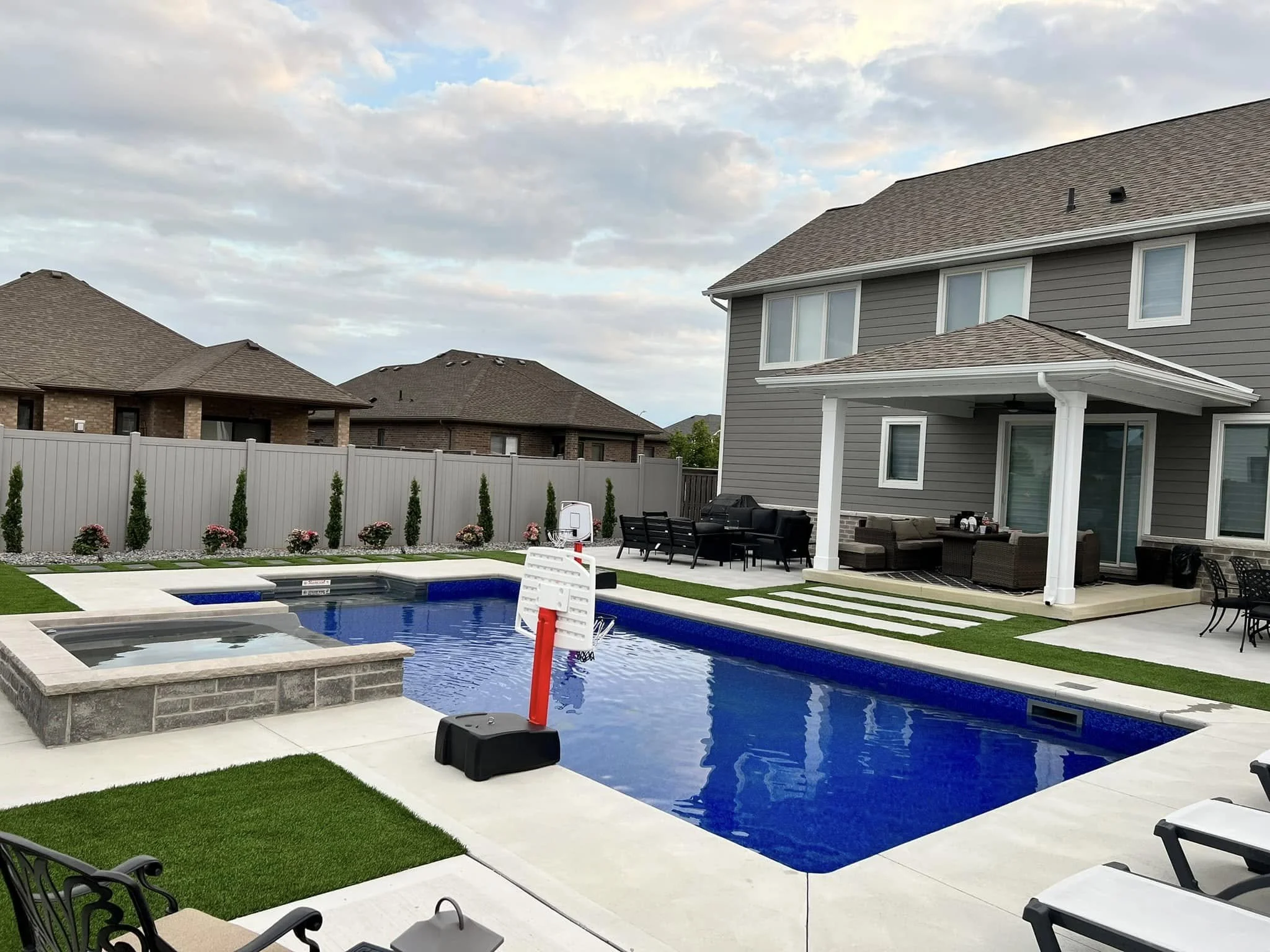 Backyard with blue inground swimming pool, hot tub, concrete pool deck, and a house with a covered porch.