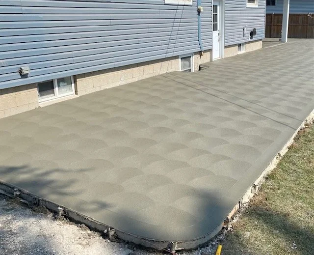 Newly poured concrete patio with a spin patterned finish next to a blue house with a white door.