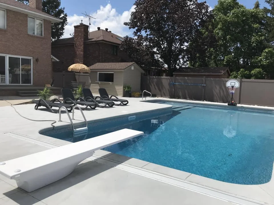 Residential backyard with a swimming pool, lounge chairs, an umbrella, a small shed, and a basketball hoop.