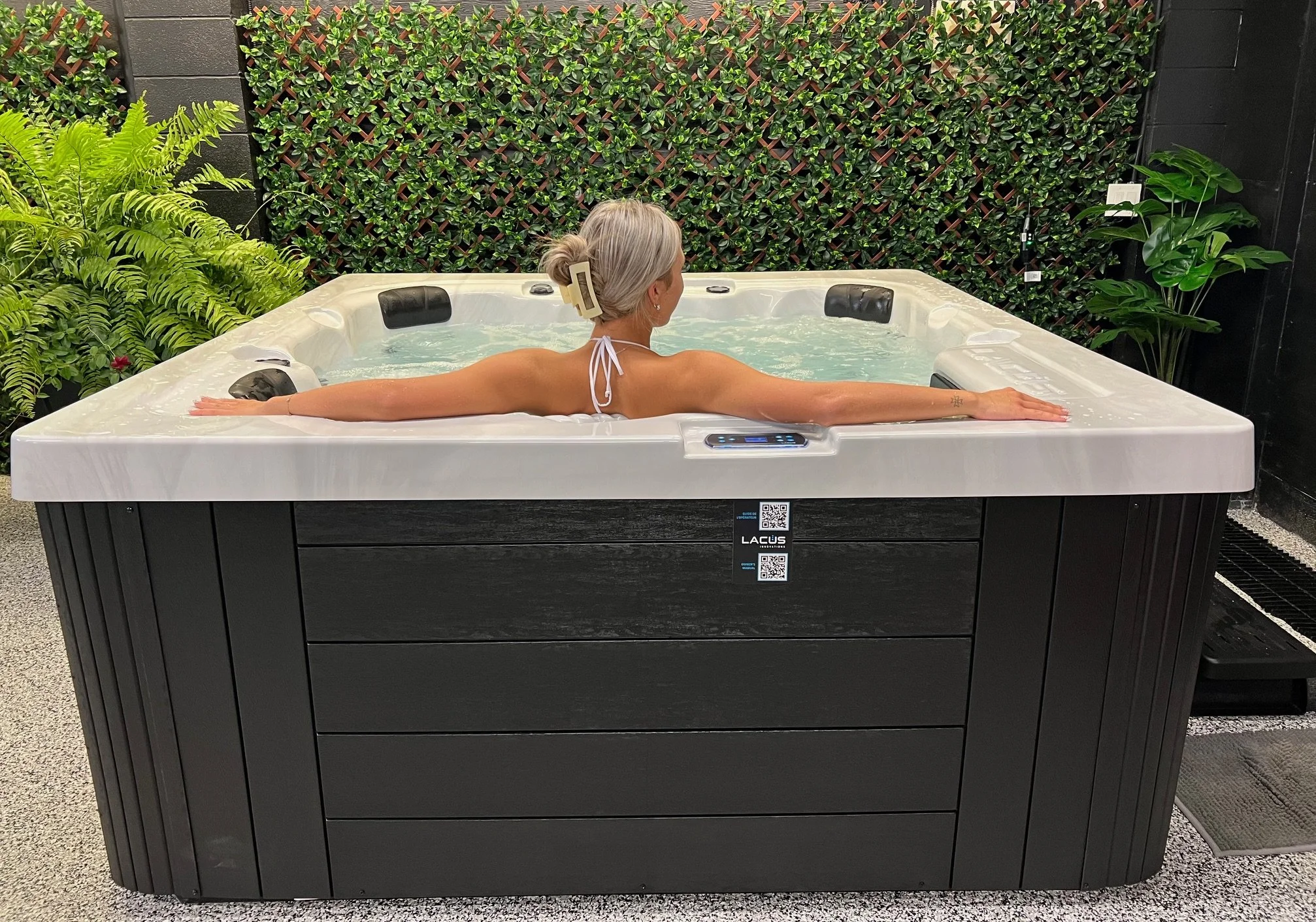 A woman with blonde hair in a bun enjoying a hot tub, sitting with arms outstretched, in hot tub store showroom in WIndsor Ontario Canada.