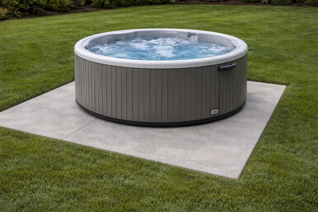 Round hot tub with water jets on a concrete pad in a grassy backyard