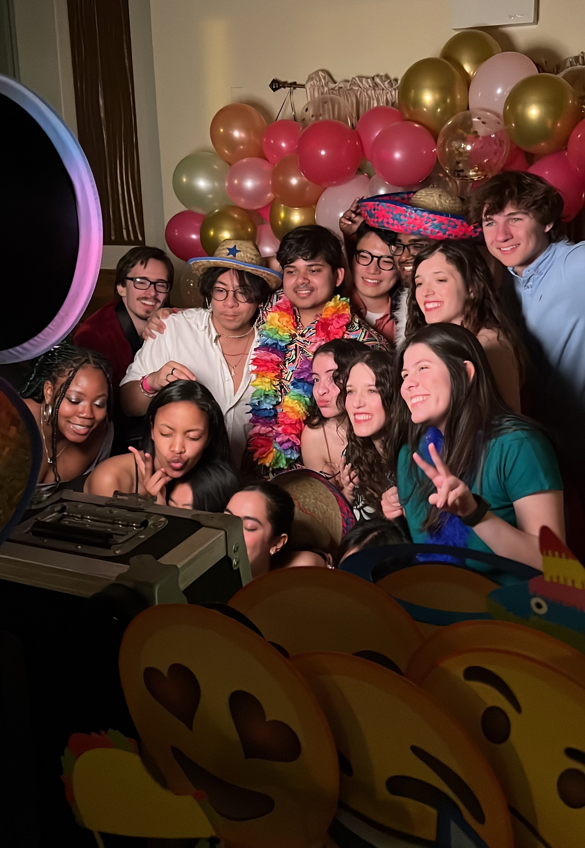 A group of people at a celebration party with balloons, some wearing festive hats, and posing for a photo.