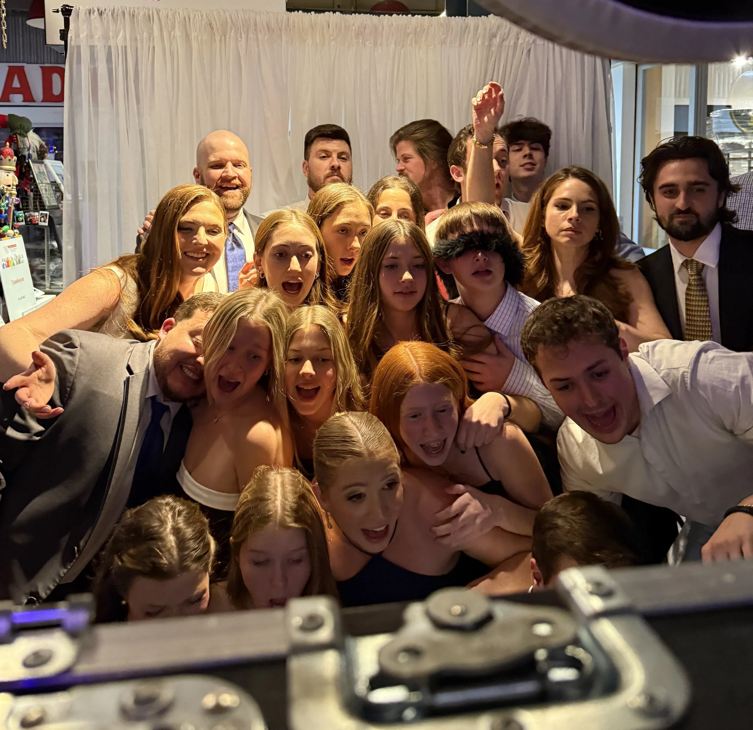 People gathered closely together, posing for a photo at an event or celebration. The group includes both men and women, some smiling, some making expressive faces, indicating a lively and cheerful atmosphere.