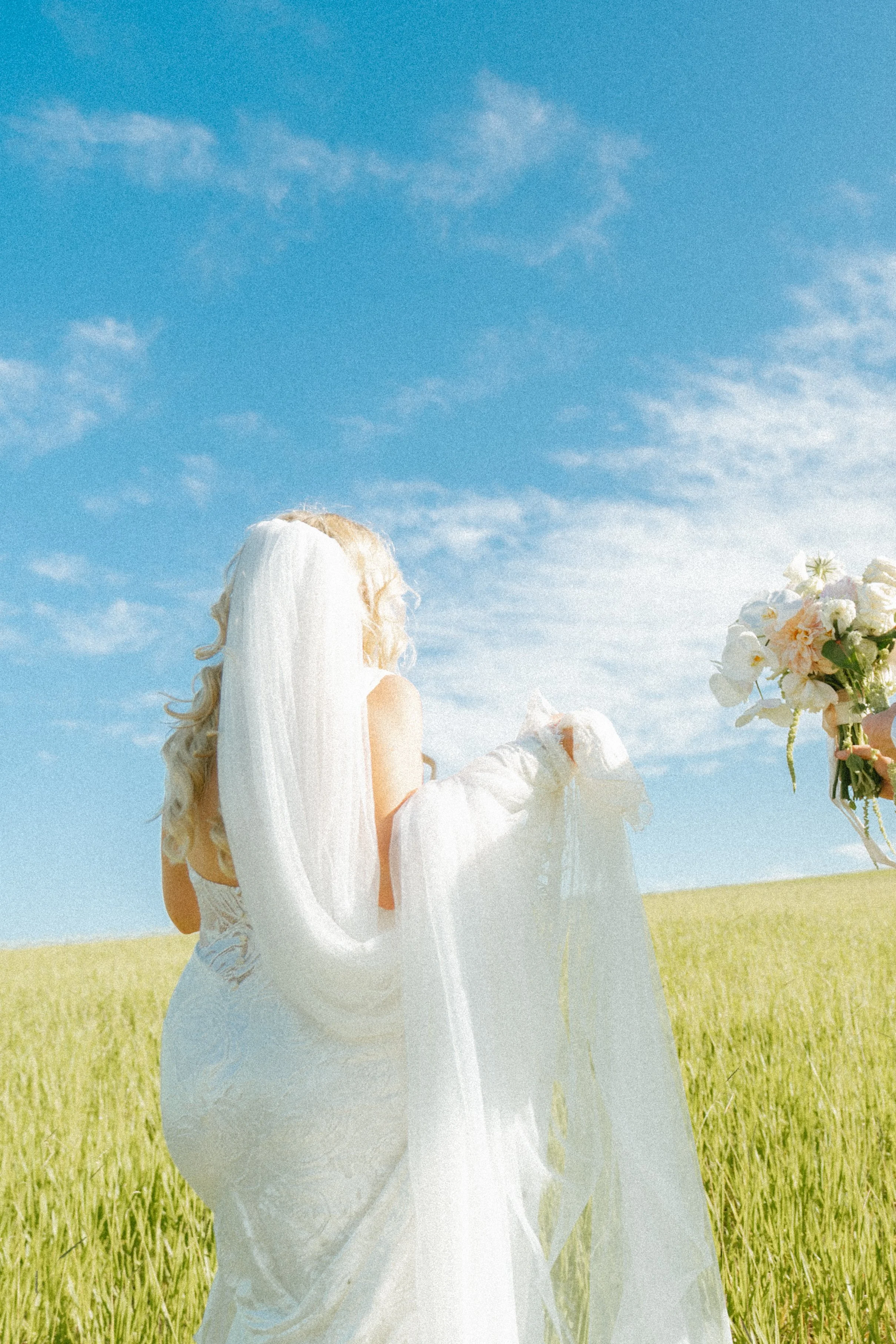 A woman dressed as a bride holding a bouquet in a green field under a blue sky