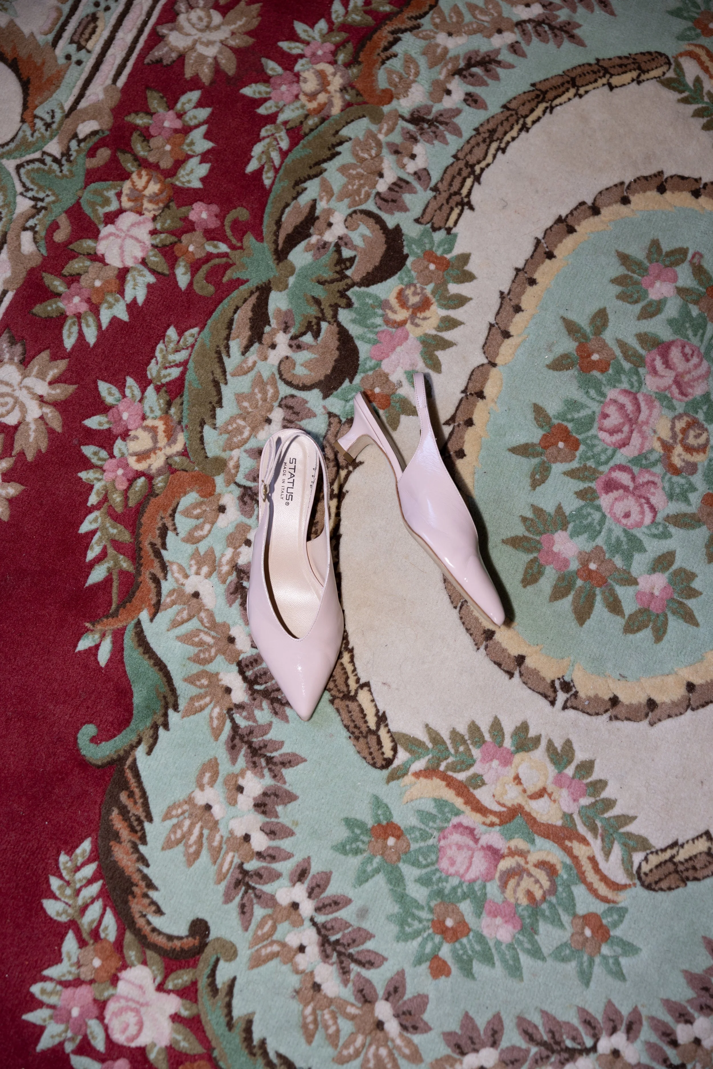 A pair of pink high-heeled shoes on an ornate floral patterned carpet.