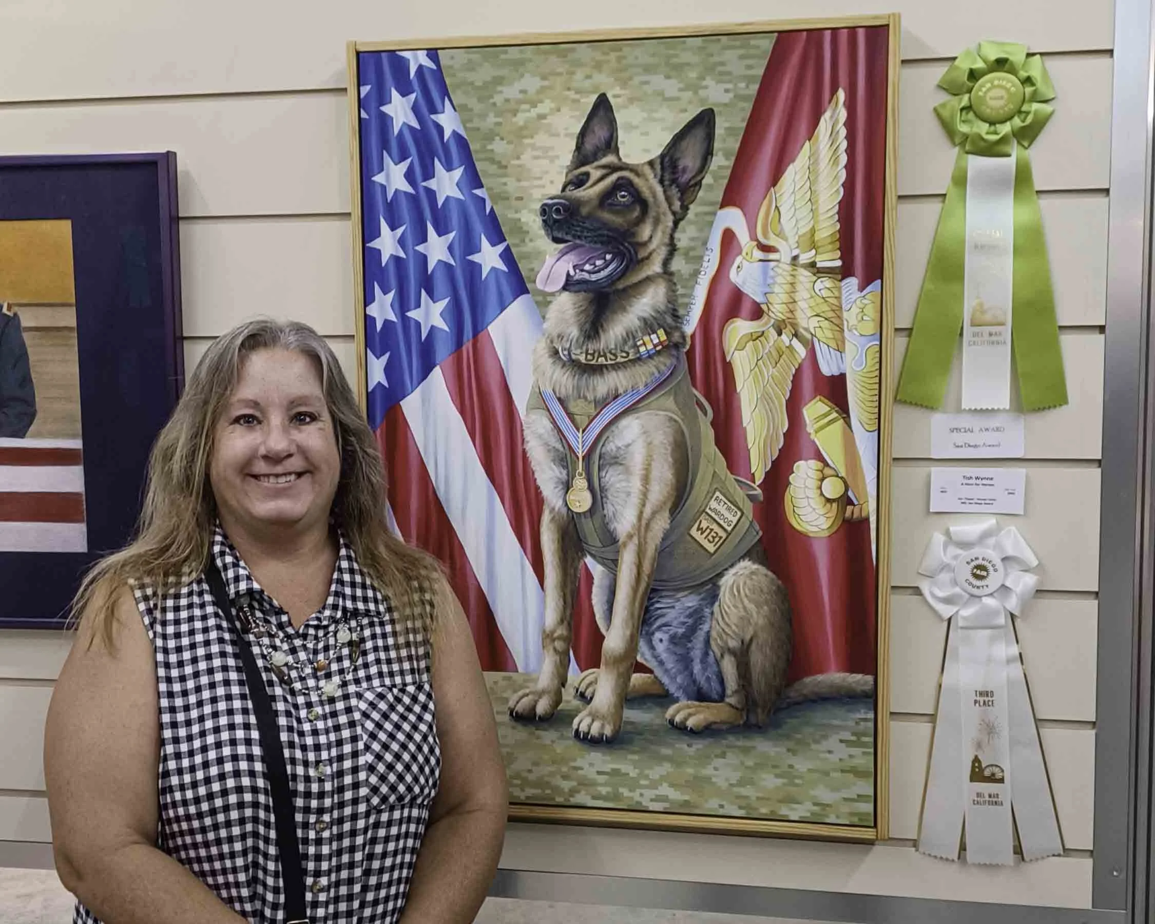Woman smiling in front of a painting of a military dog with the American flag and a marines flag in the background, surrounded by award ribbons.