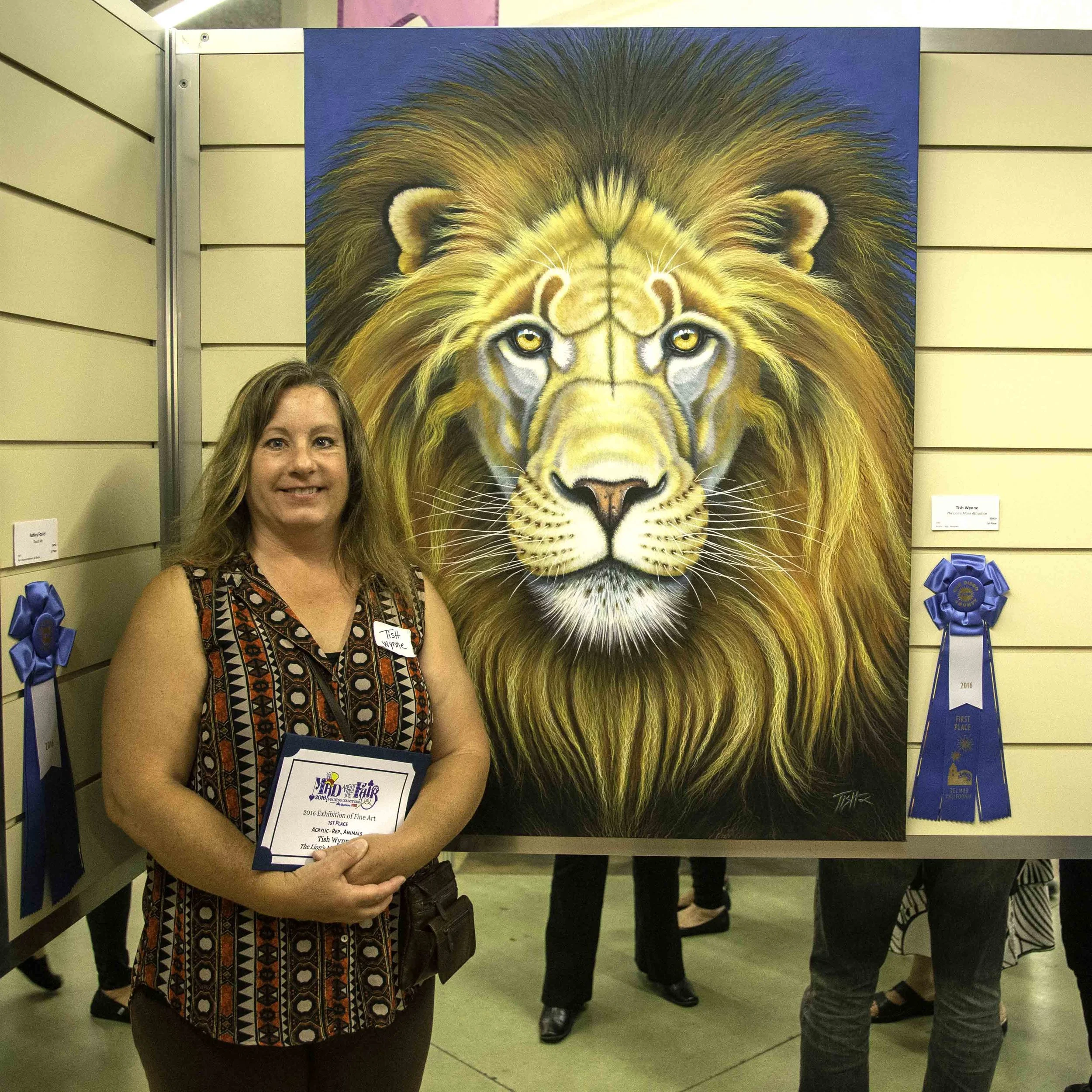 A woman standing in front of a large, colorful painting of a lion with a thick mane. She is holding a certificate award. There is a blue ribbon attached to the wall on either side of the painting, indicating an award or recognition event.