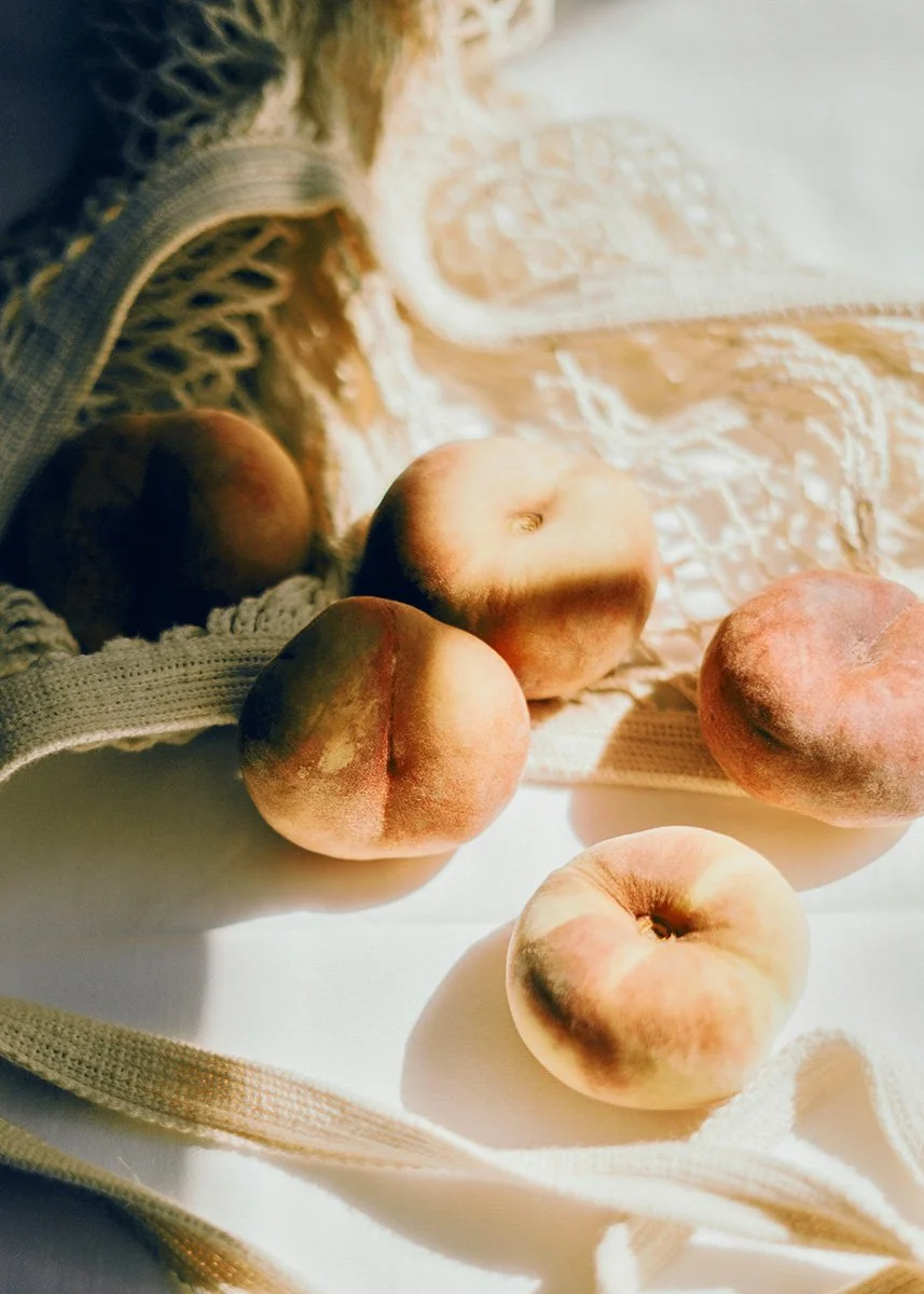 Five peaches resting on a fabric surface with sunlight casting shadows.