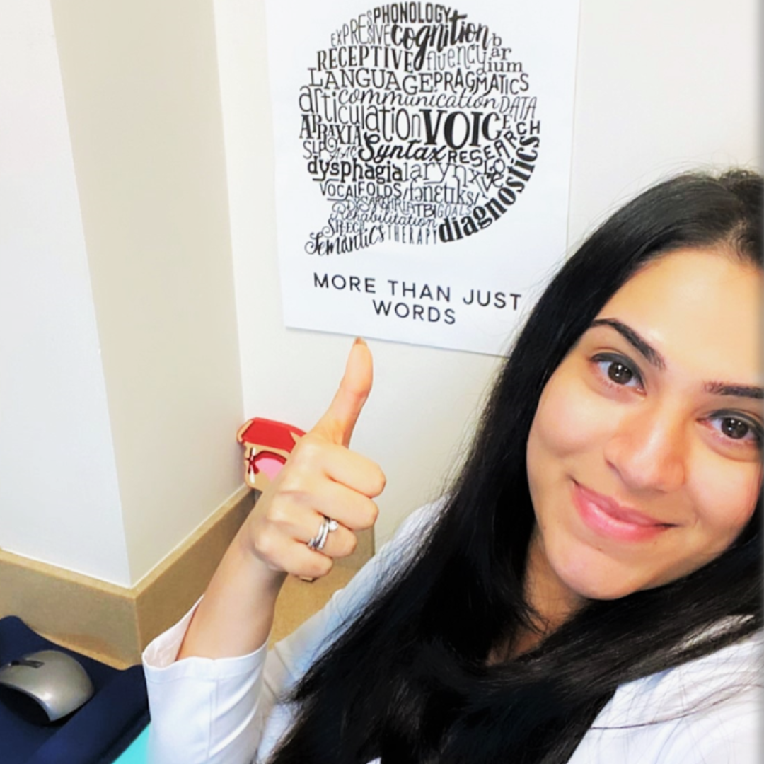 Woman smiling and pointing at a poster on the wall with words related to speech therapy, with the phrase 'More Than Just Words'