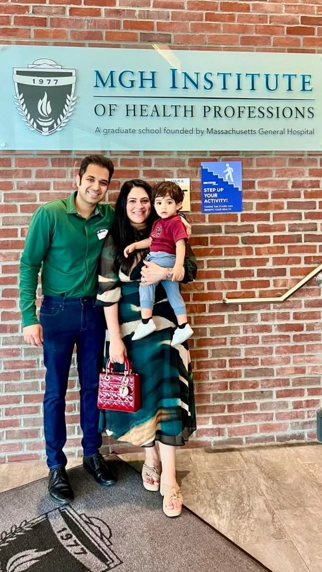 Rinki Varindani Desai and family standing in front of a brick wall and a sign that reads 'MGH Institute of Health Professions.'