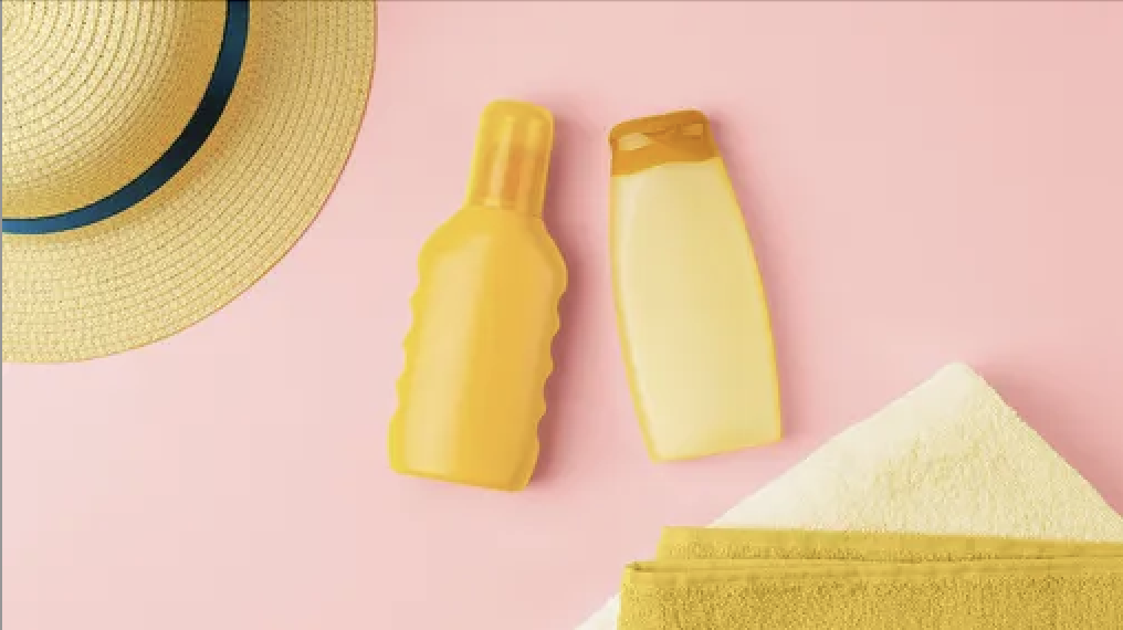 A yellow hat, sunscreen bottle, and towel sit against a pink background.