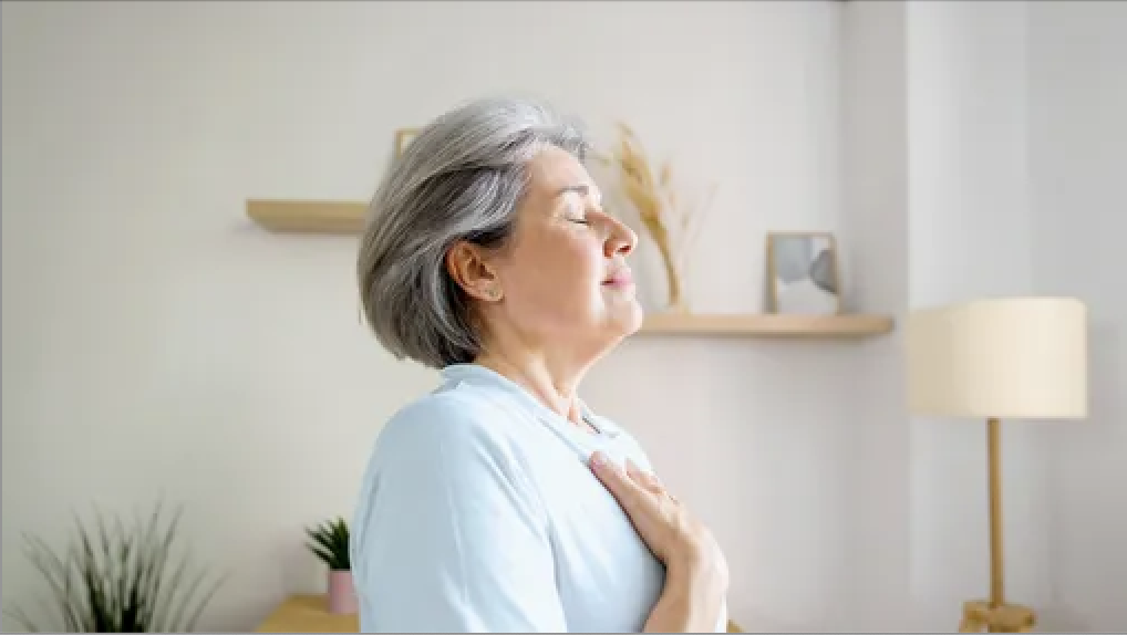 A woman stands with her hand on her chest.