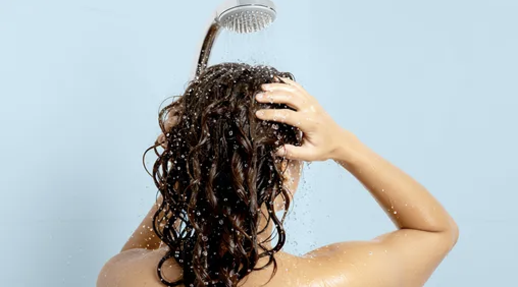 A woman scrubs her hair in the shower.