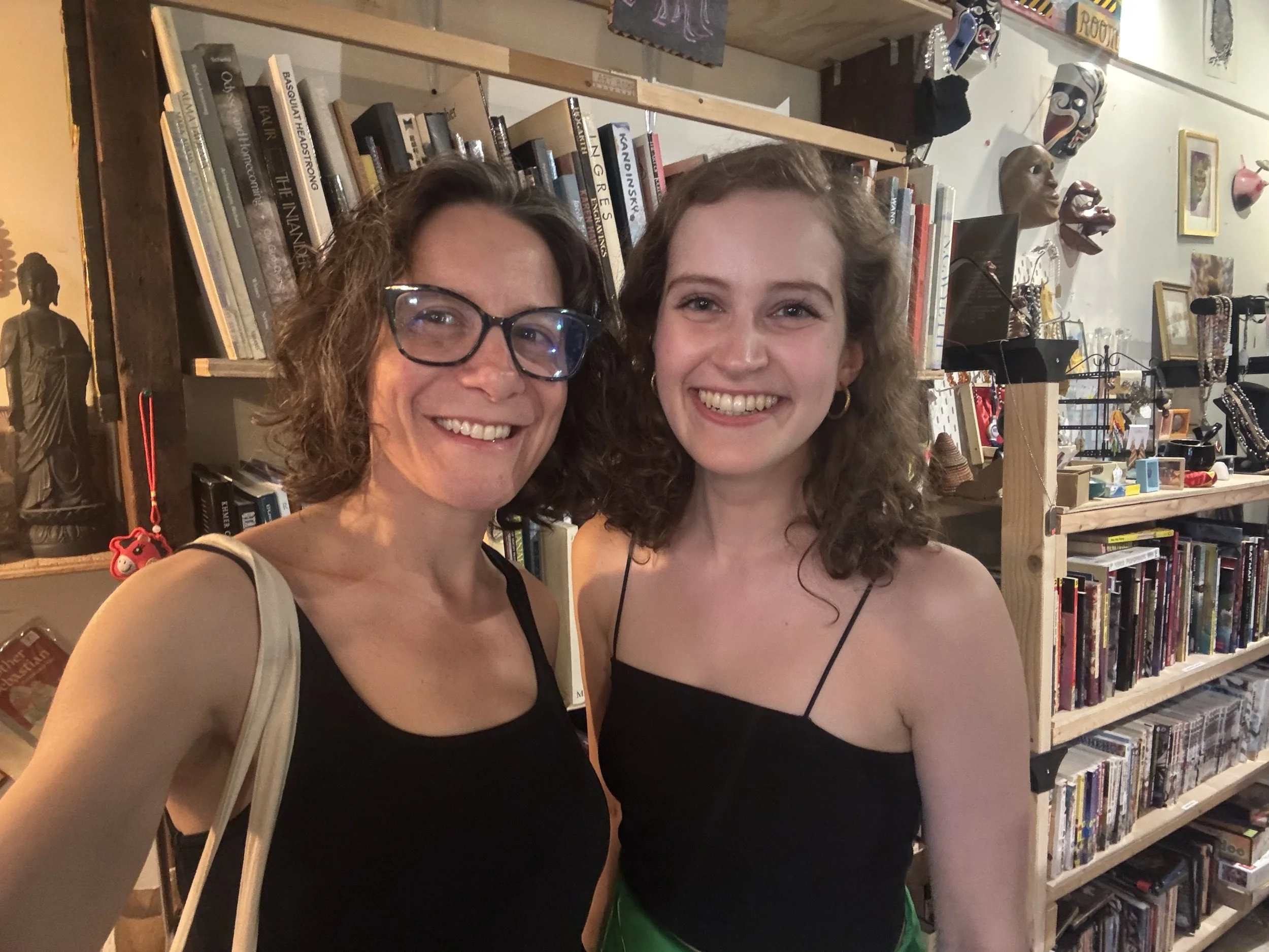 Jacqueline and her friend stand smiling in front of bookshelves.