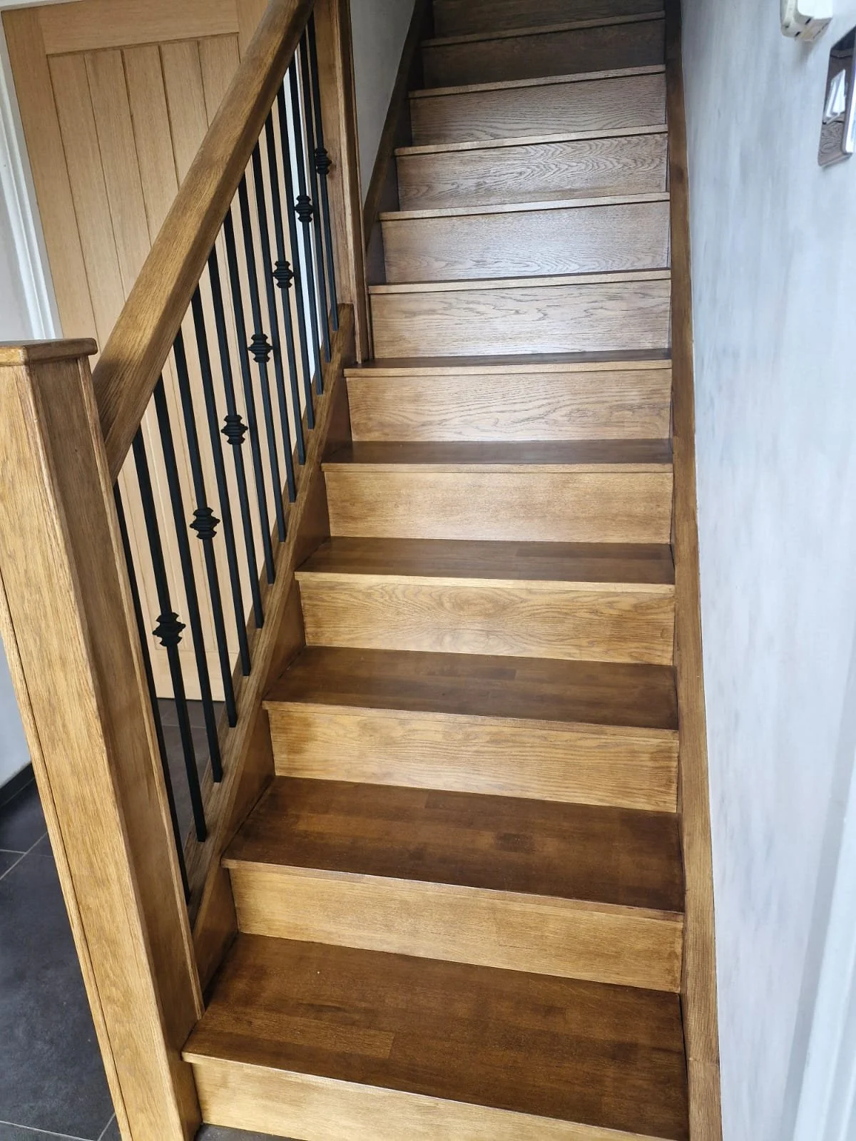 Wooden staircase with black metal balusters and handrail in a home interior.