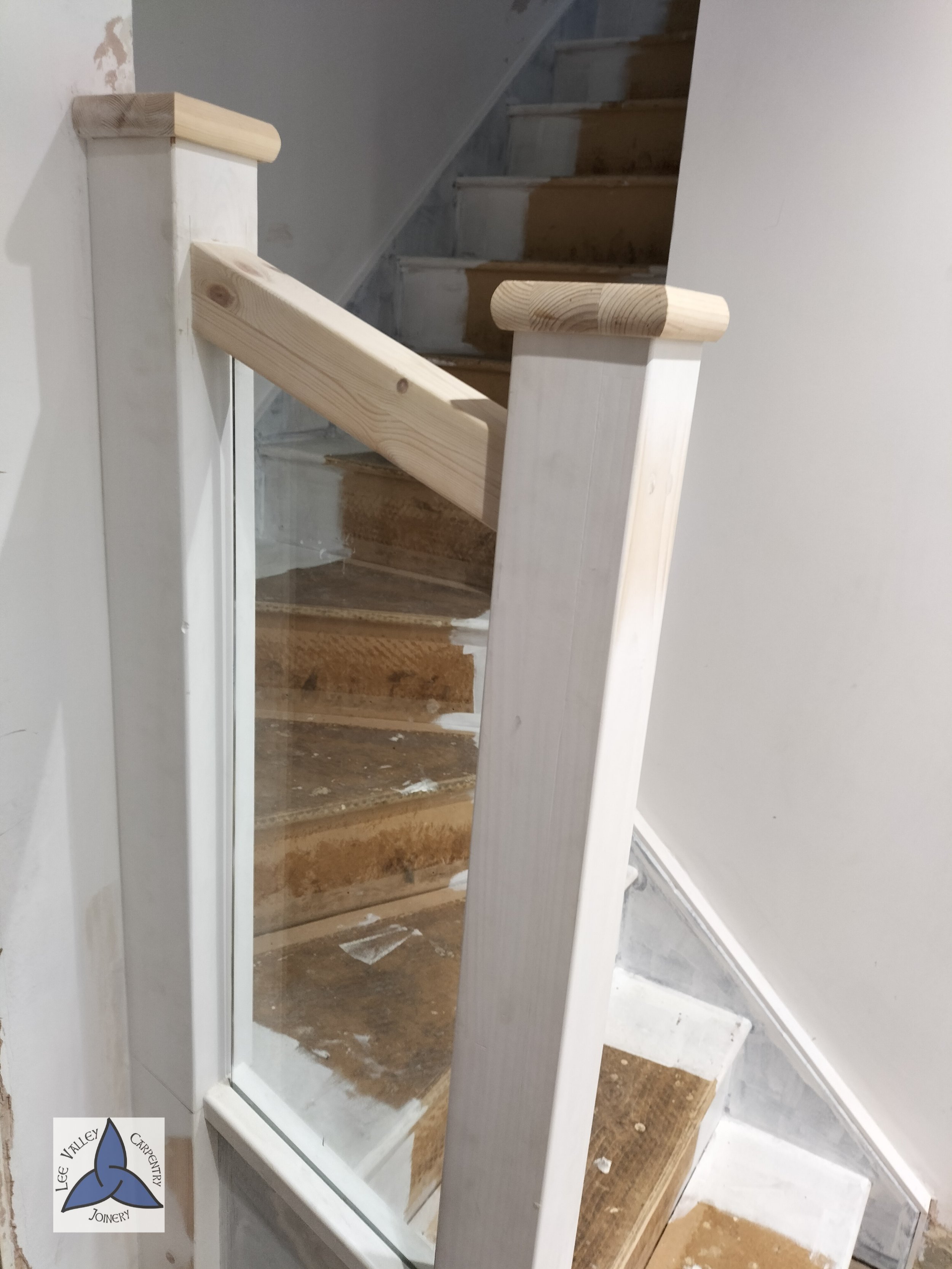 A staircase with unfinished wooden steps and white wooden railing, partially painted wall, and construction materials visible.