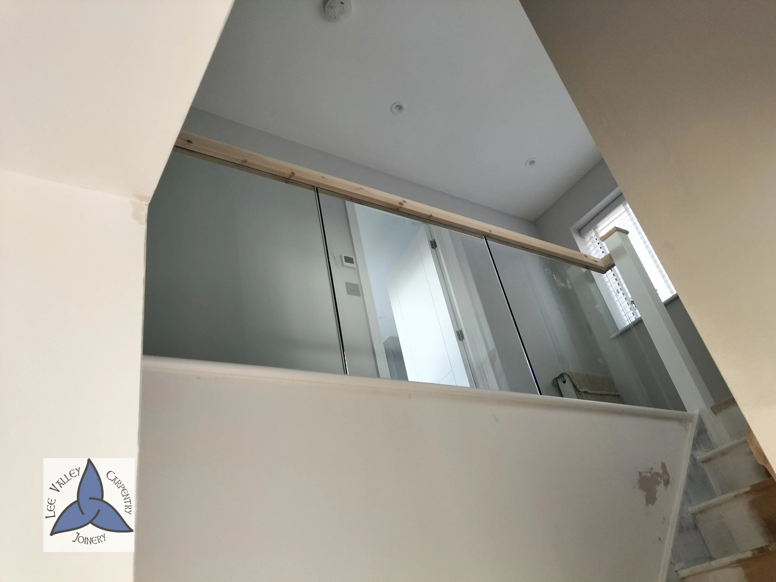 Interior of a house under construction or renovation, showing a glass railing, stairs, and a window with blinds.